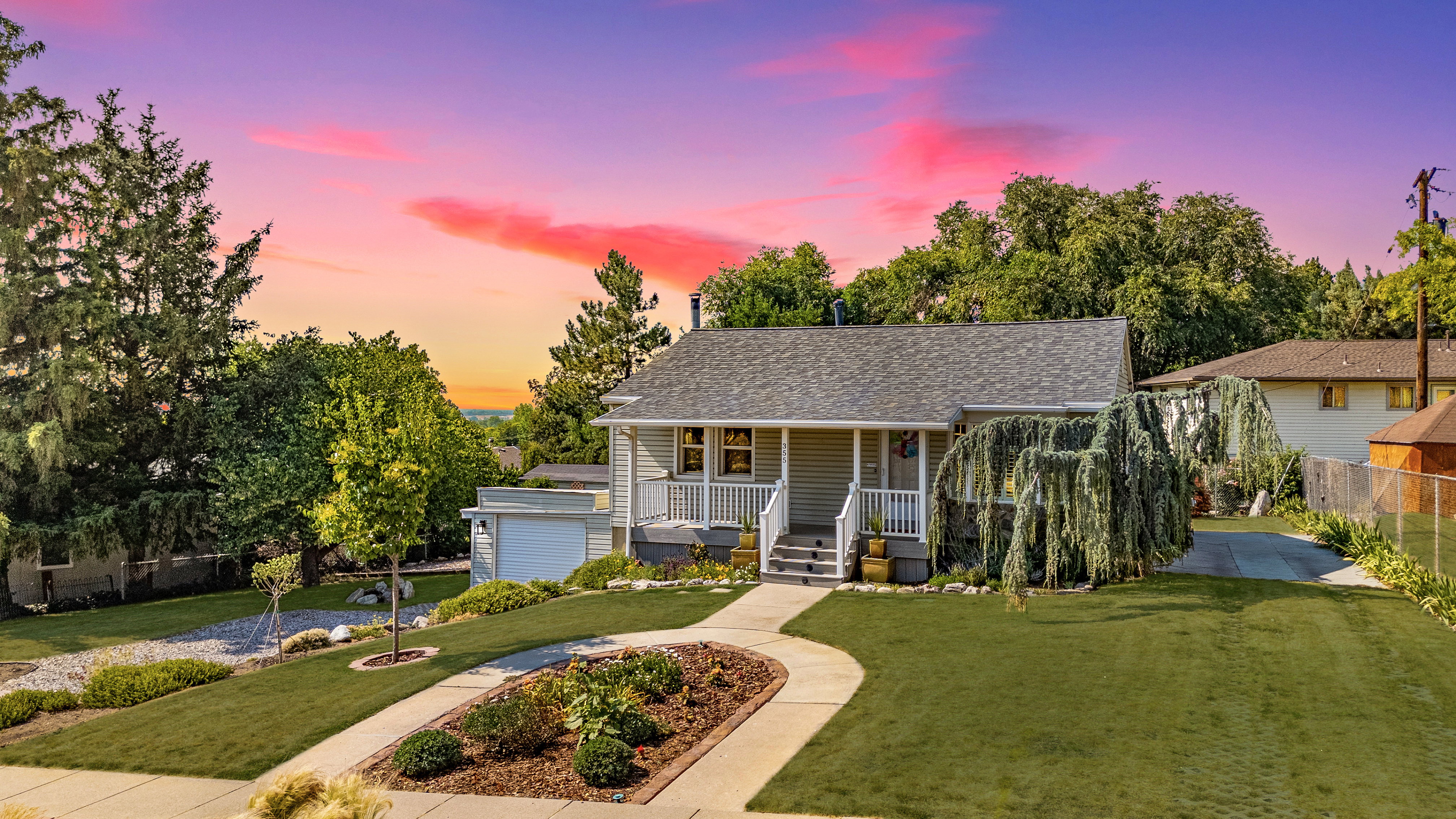 Charming residence featuring a welcoming front porch with white railing, a meticulously manicured lawn, and mature trees