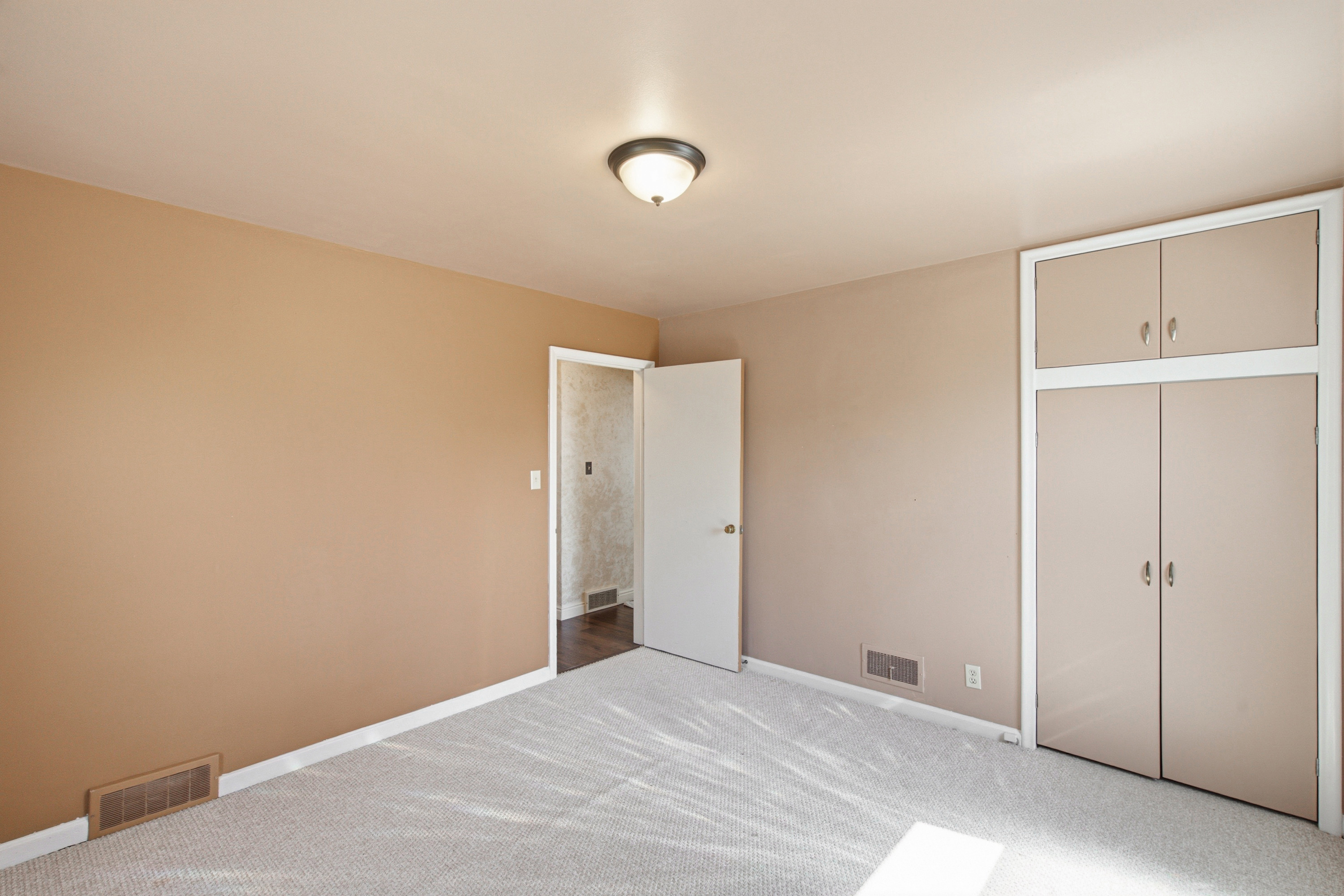Neutral-toned room featuring light-colored carpet flooring and a built-in closet with upper cabinetry