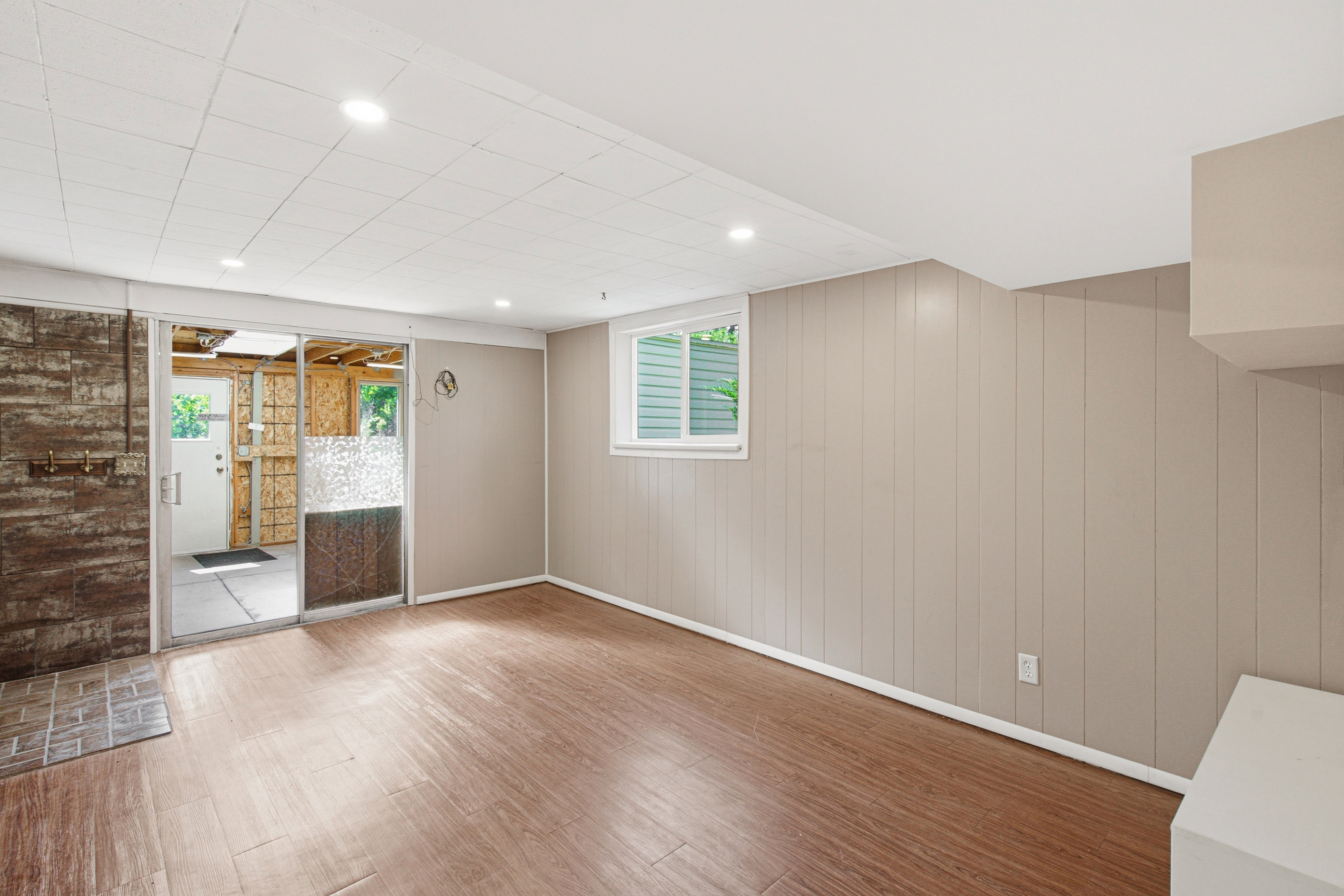 Finished lower level featuring wood-finish flooring, recessed lighting, neutral vertical paneling, and an egress window
