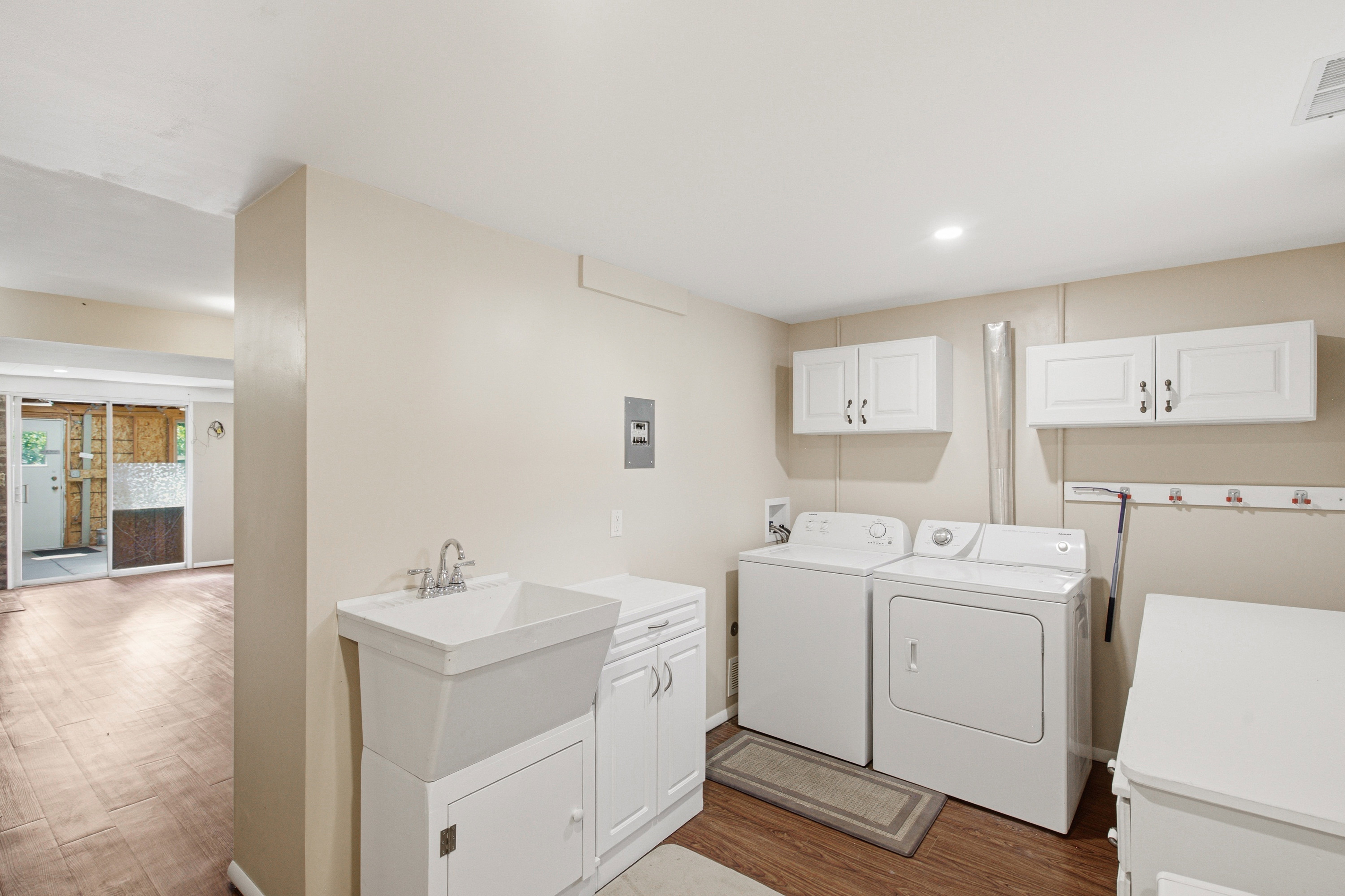 Dedicated laundry area featuring a utility sink with white cabinetry, wood-finish flooring, recessed lighting, and wall-mounted white storage cabinets
