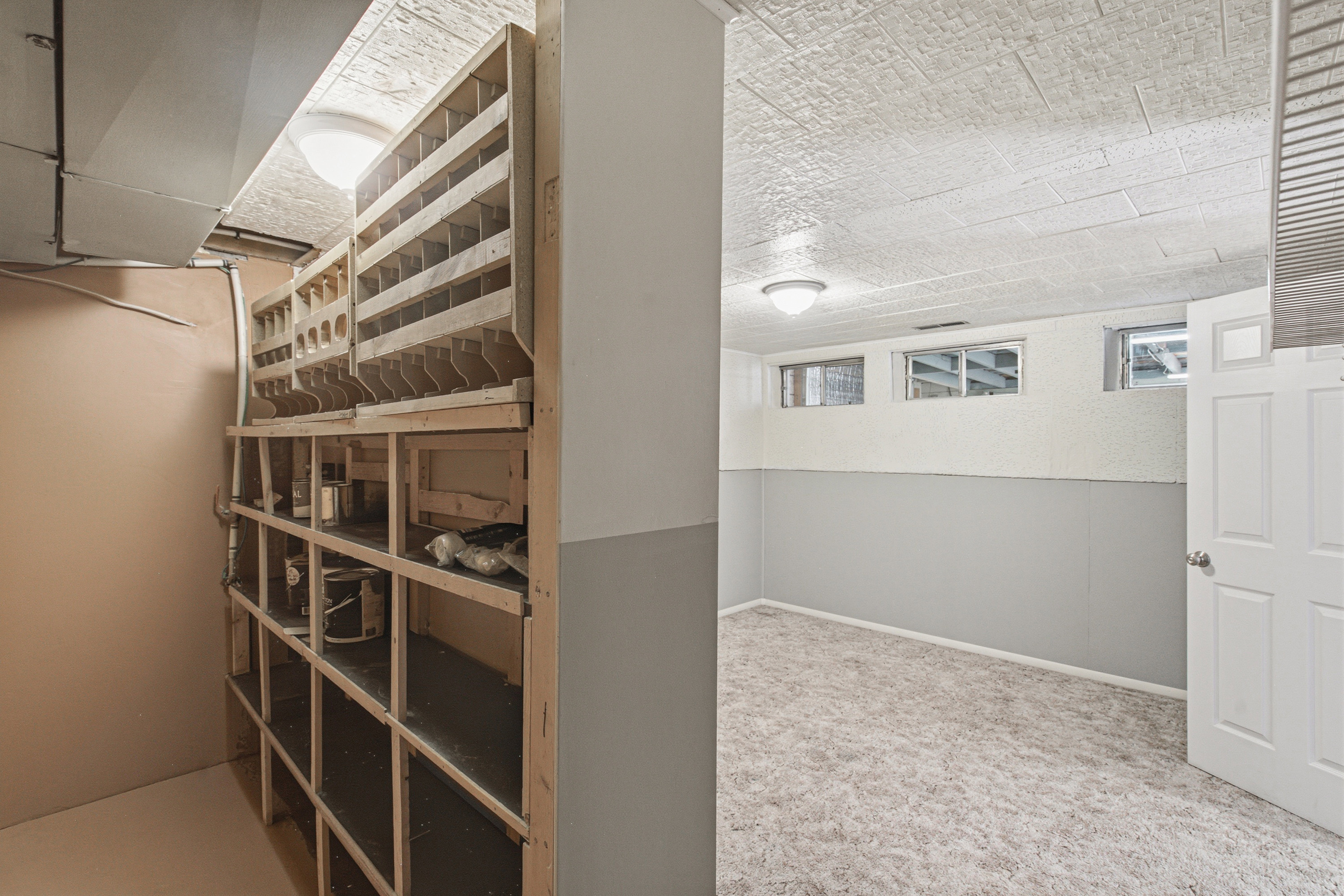 Versatile basement area featuring wood shelving, recessed windows, textured ceiling, a white paneled door, and carpet flooring