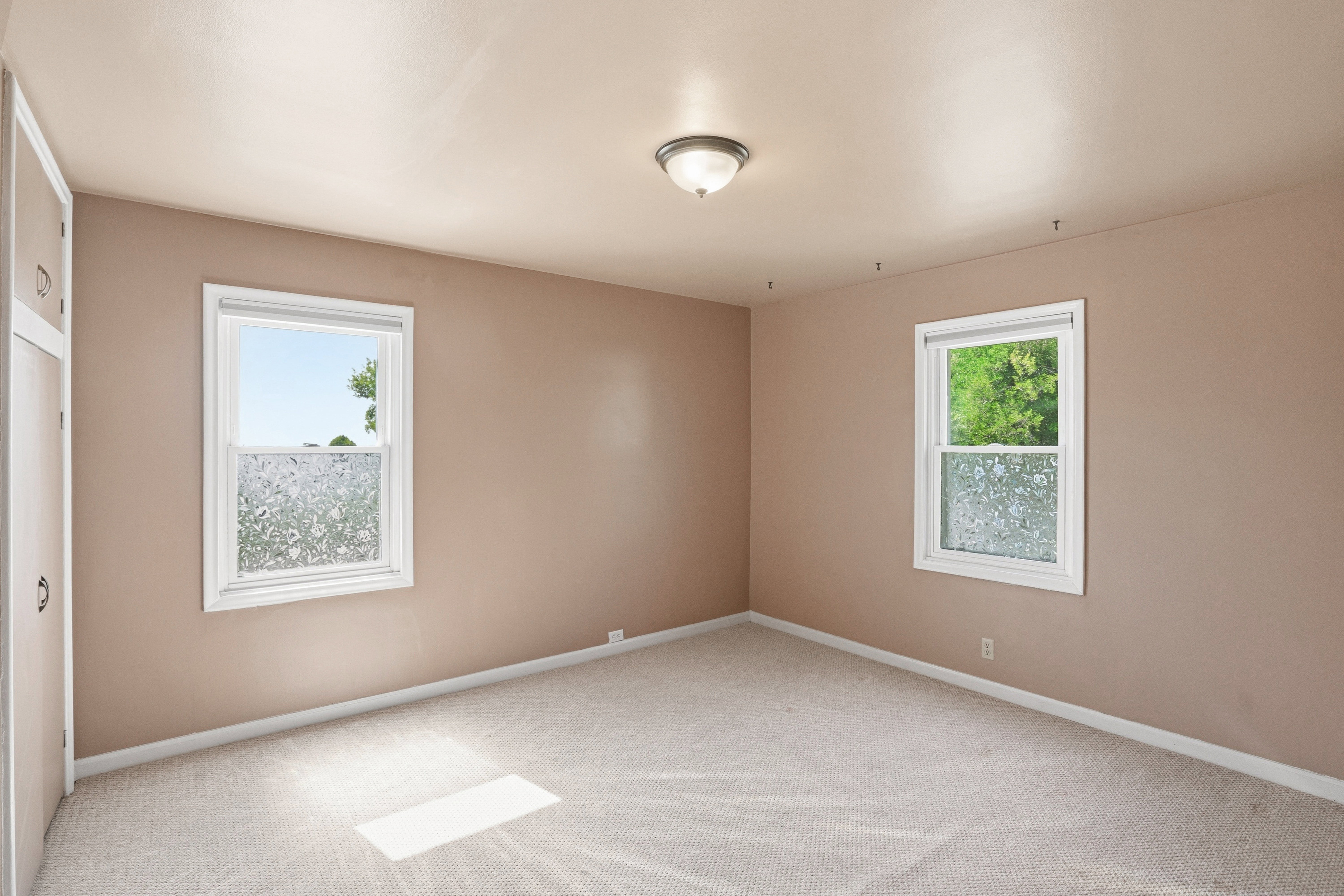 Carpeted room featuring two windows with white trim, built-in cabinetry, and a ceiling-mounted light fixture