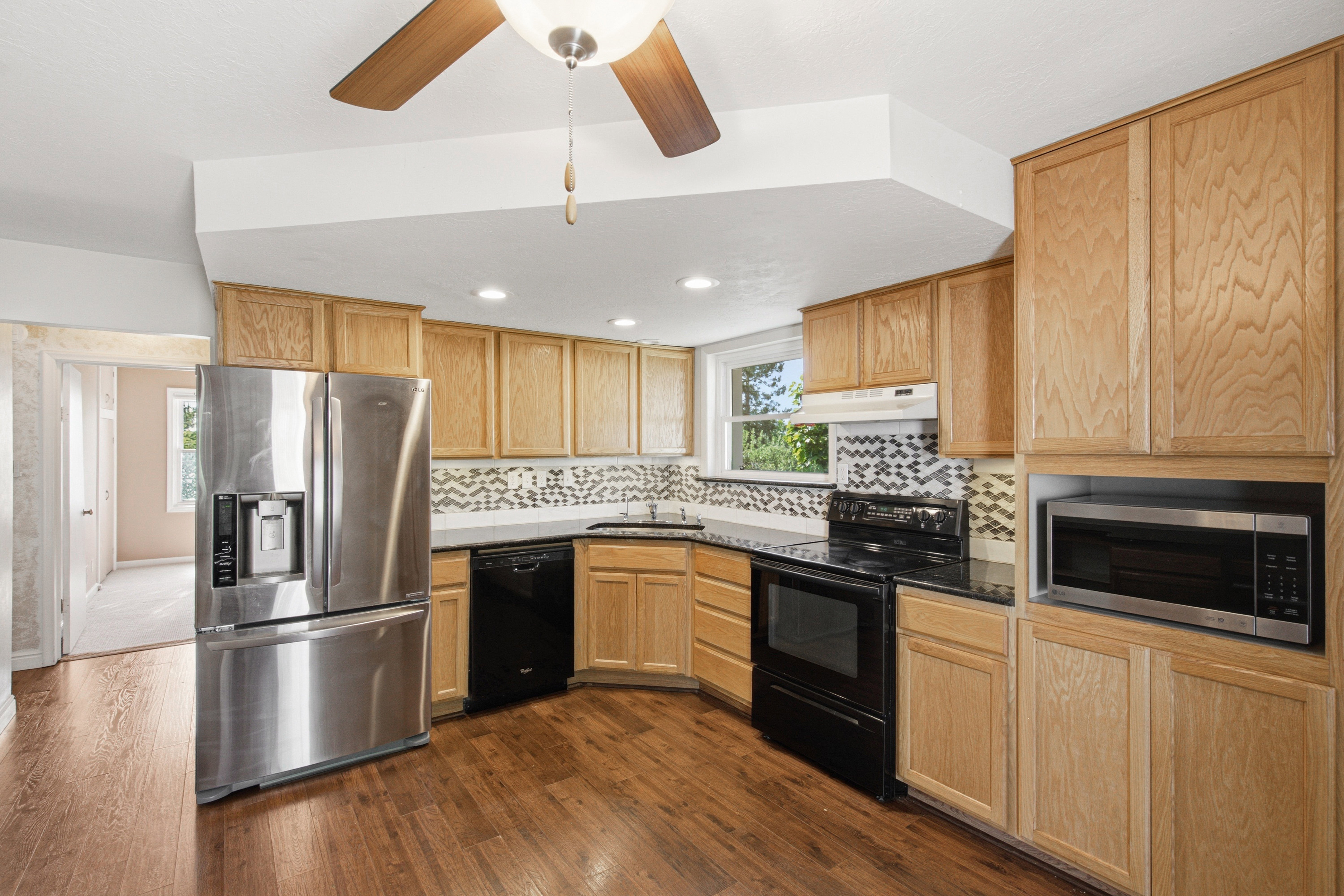 Kitchen featuring wood-finish flooring, light wood cabinetry, black countertops, and a patterned tile backsplash