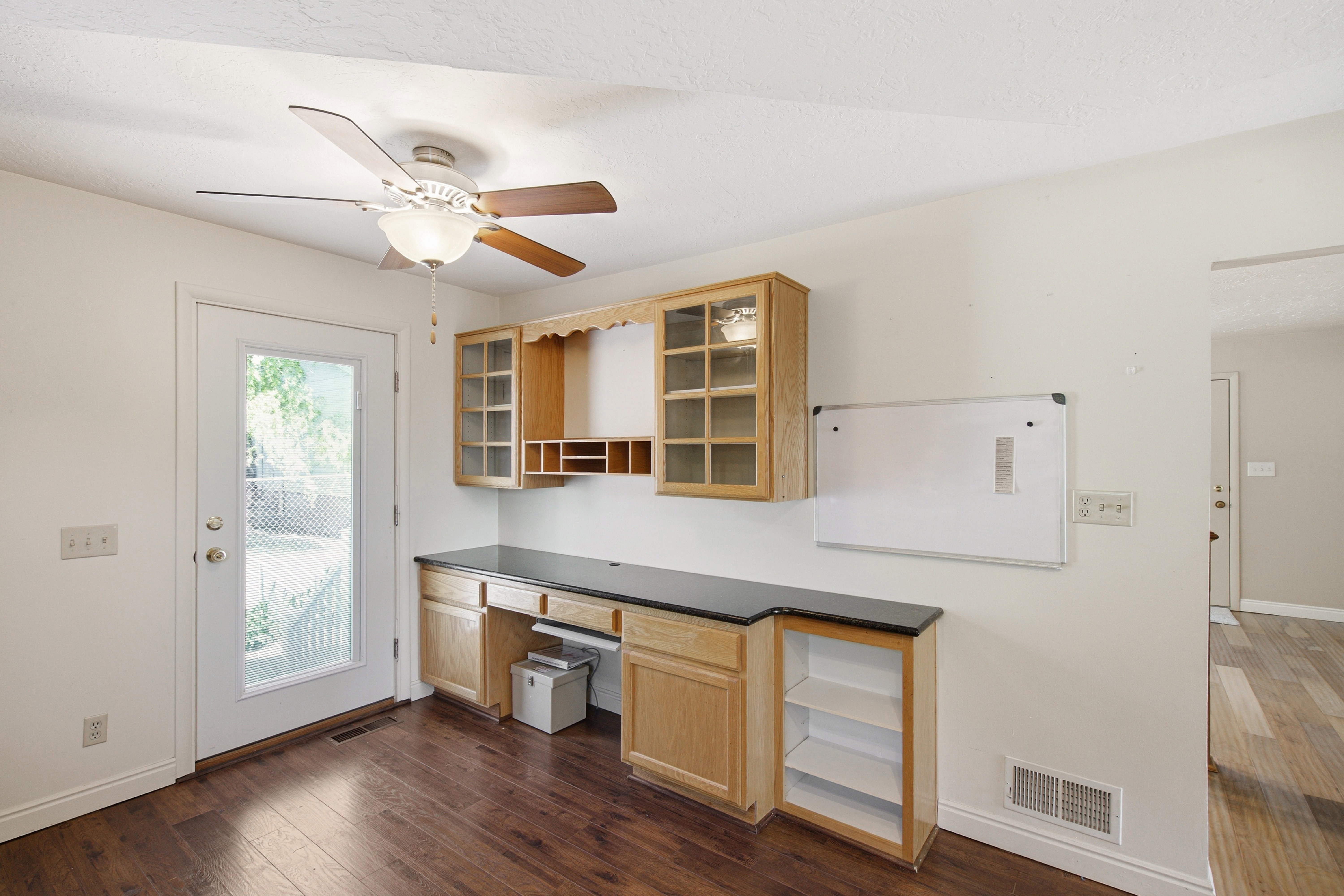 Dedicated workspace featuring built-in light wood cabinetry with glass fronts, dark countertops, and integrated desk space