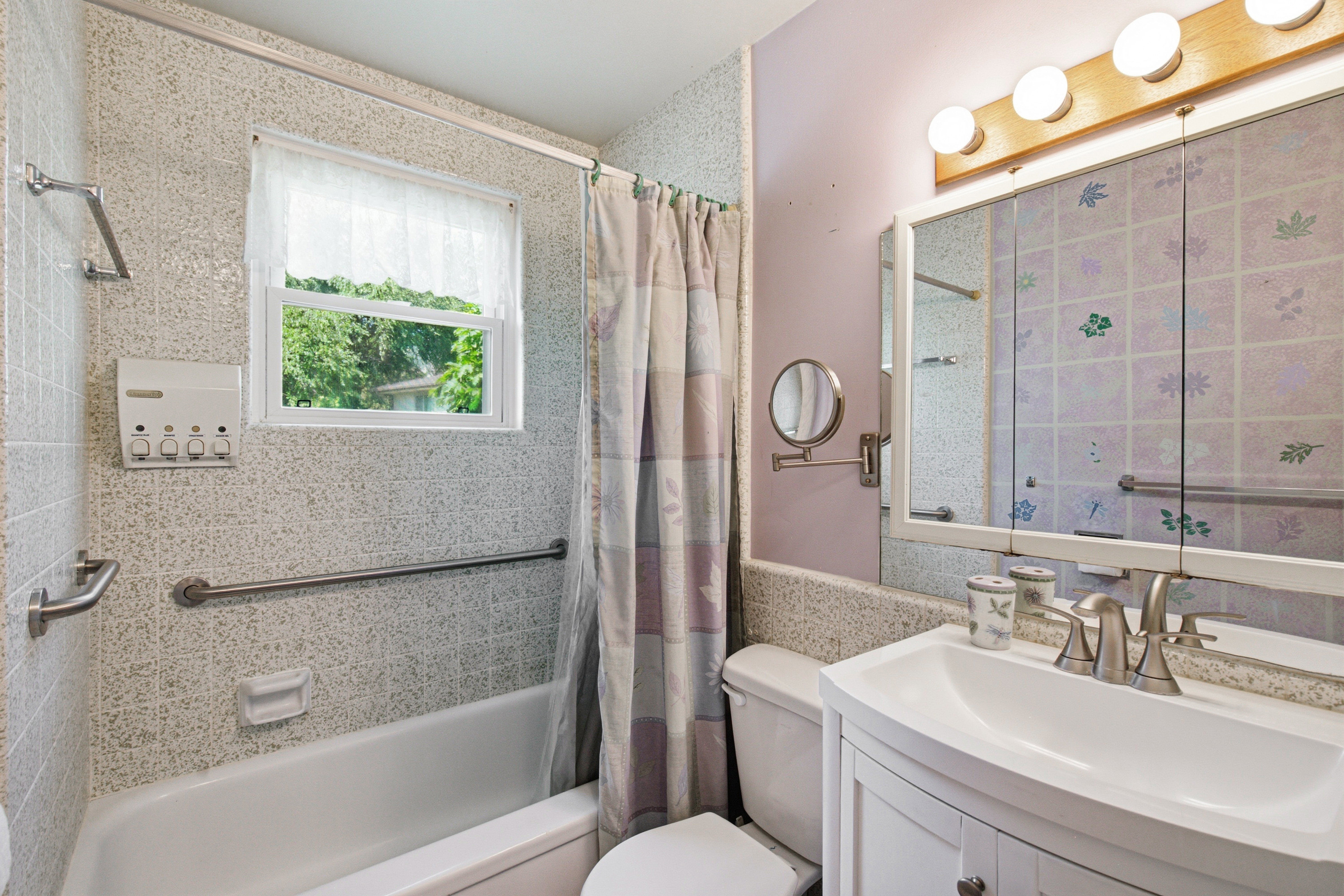 Bathroom featuring a white bathtub with tile surround, a window with privacy curtain, and a vanity with an integrated sink and base cabinet