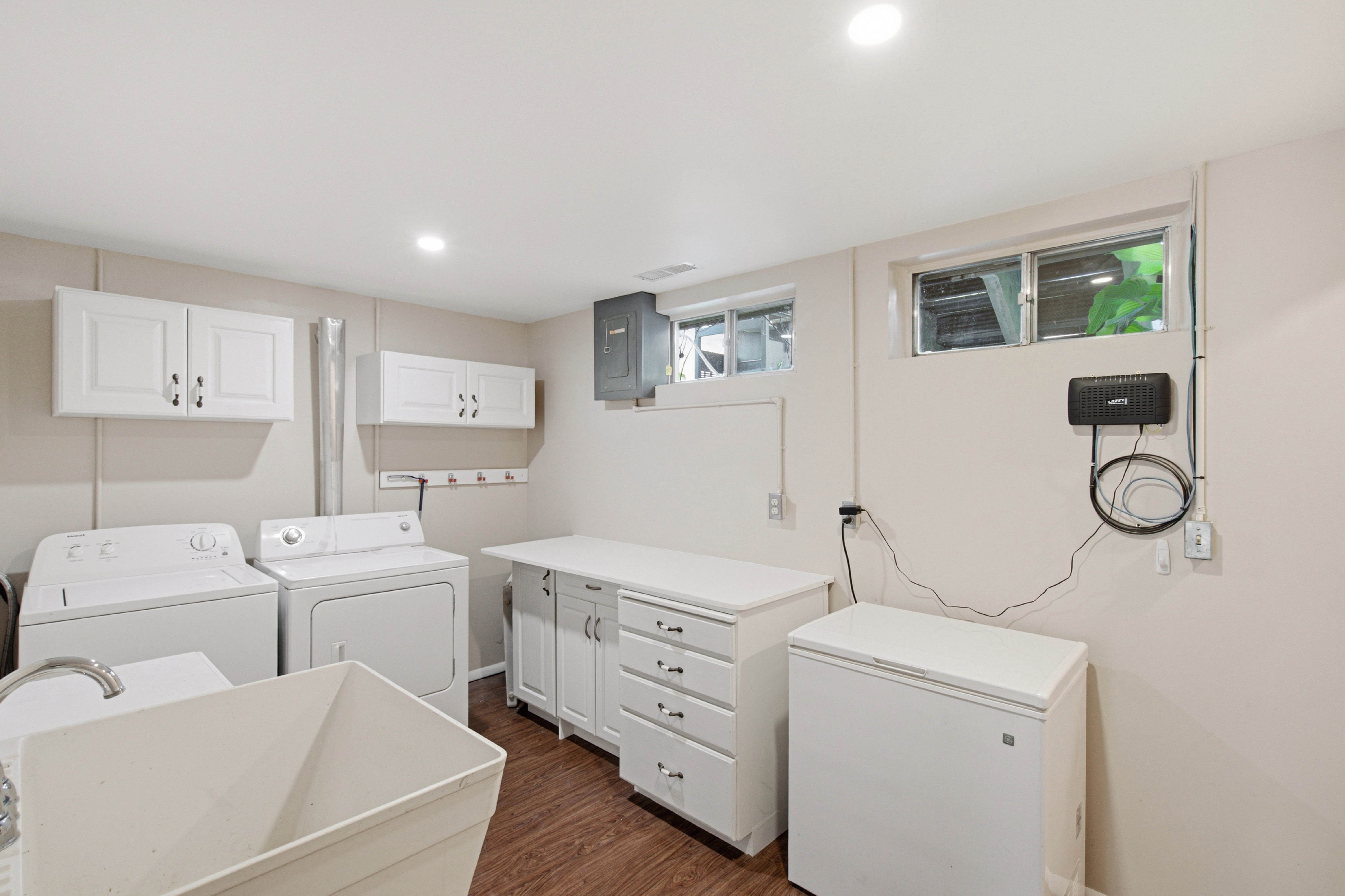 Laundry room featuring a utility sink, wood-finish flooring, two upper cabinets, lower cabinetry with drawers, and recessed lighting