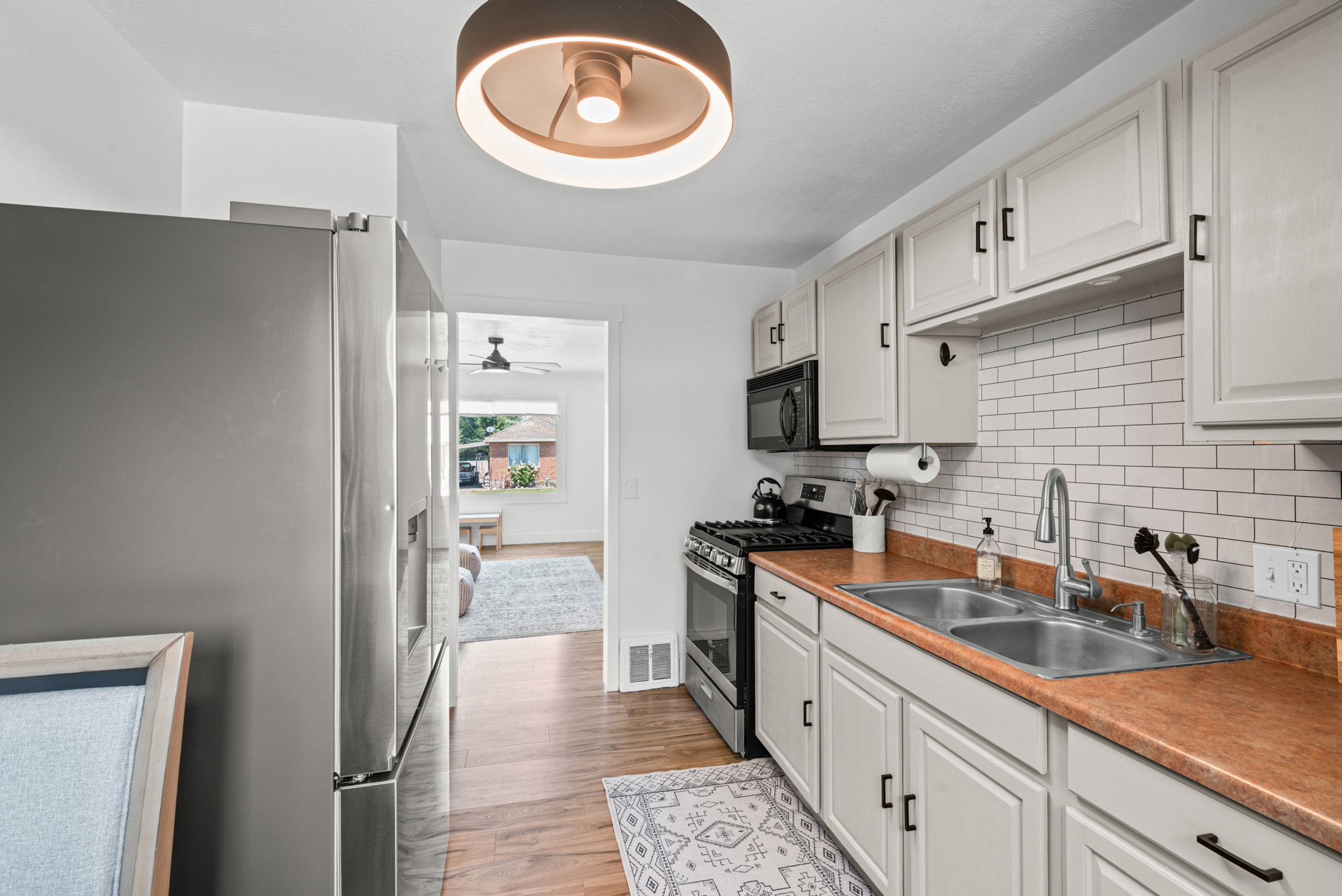 Kitchen featuring stainless steel appliances, light-toned cabinetry with dark hardware, a subway tile backsplash, and wood-finish flooring