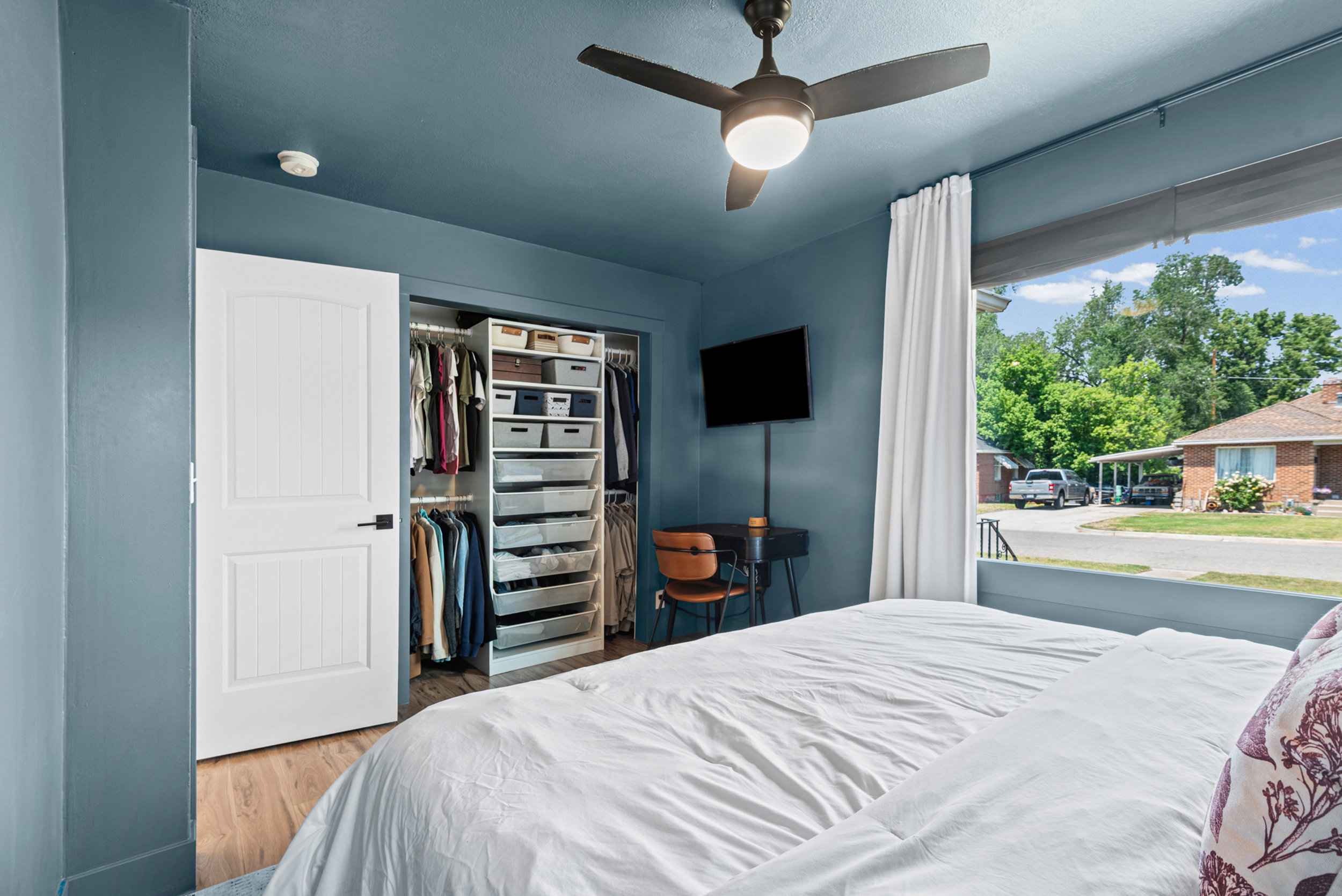 Bedroom featuring a custom closet organization system, wood-finish flooring, and a ceiling fan with integrated lighting