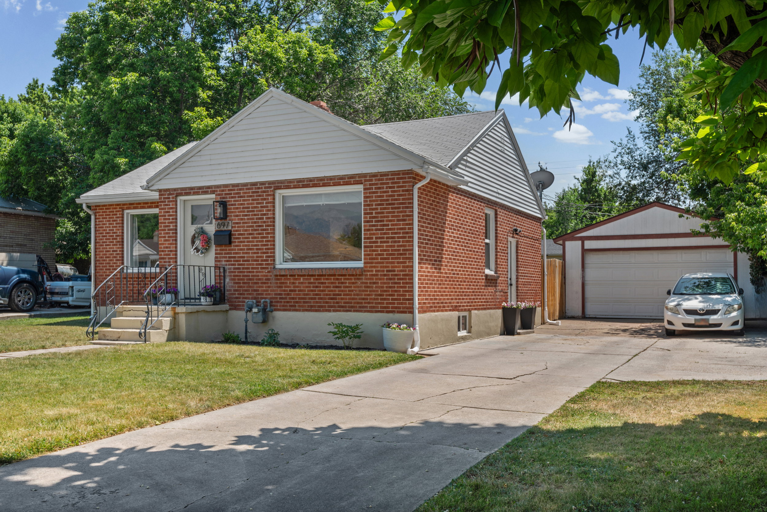 Brick exterior featuring white siding gables, an attached front porch with metal railings, a paved driveway, and a detached two-car garage with a white overhead door