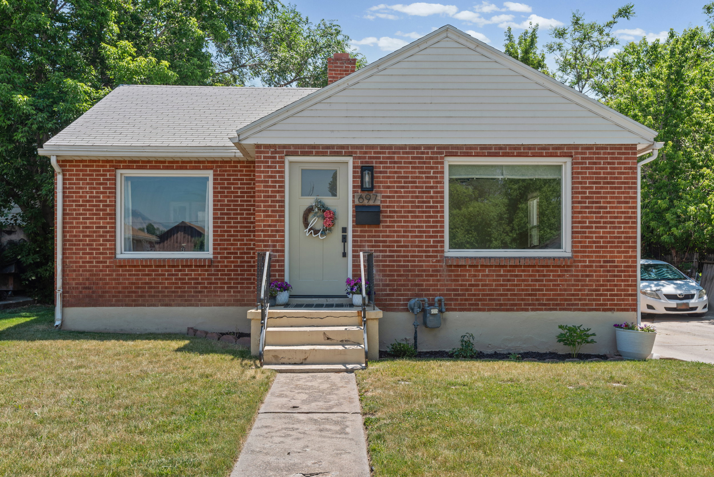Brick exterior with a white gable accent, white-framed windows, a light-colored front door, and a concrete pathway leading to steps with black railings