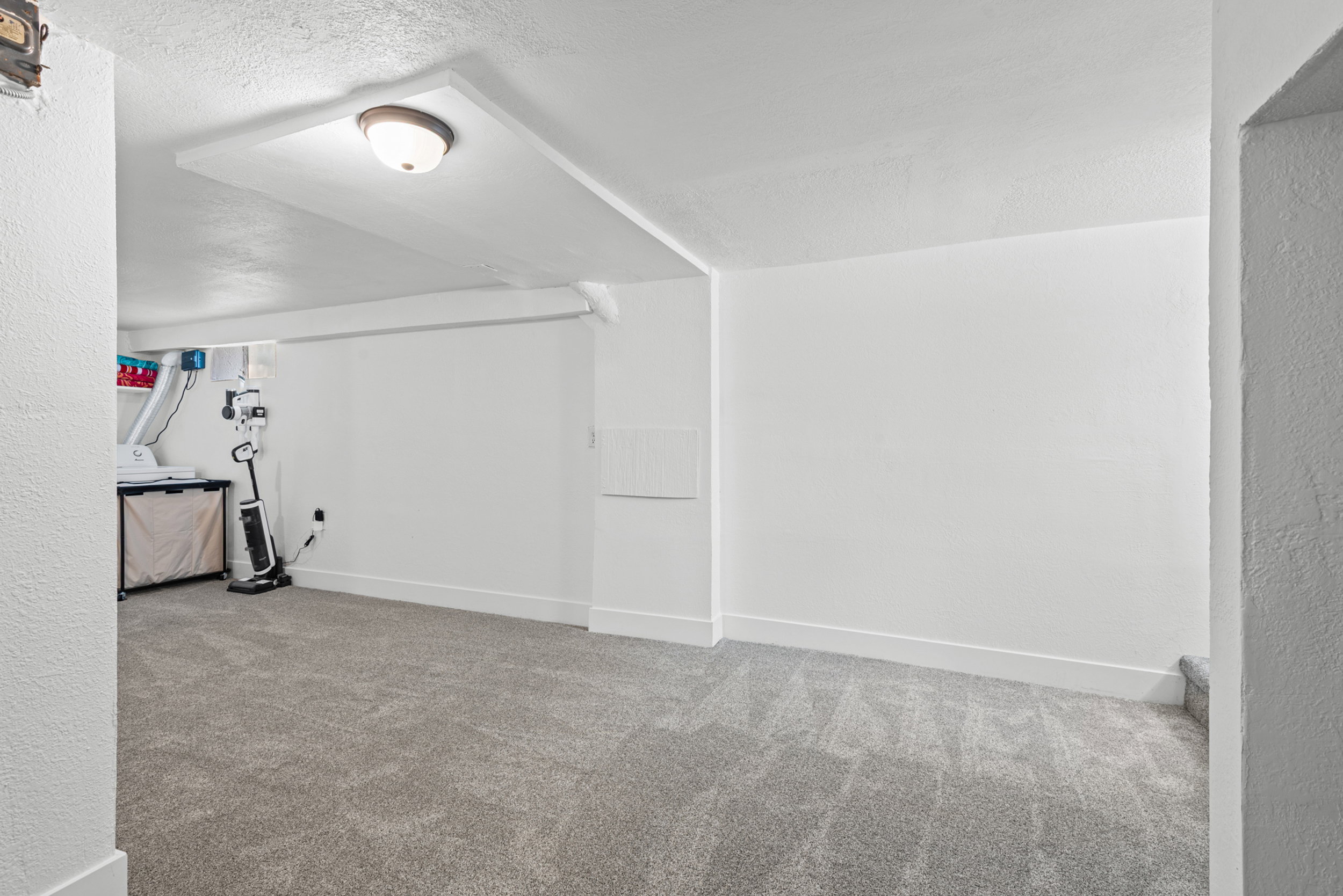 Spacious room featuring new gray carpet, white painted walls, and a flush-mount ceiling light fixture