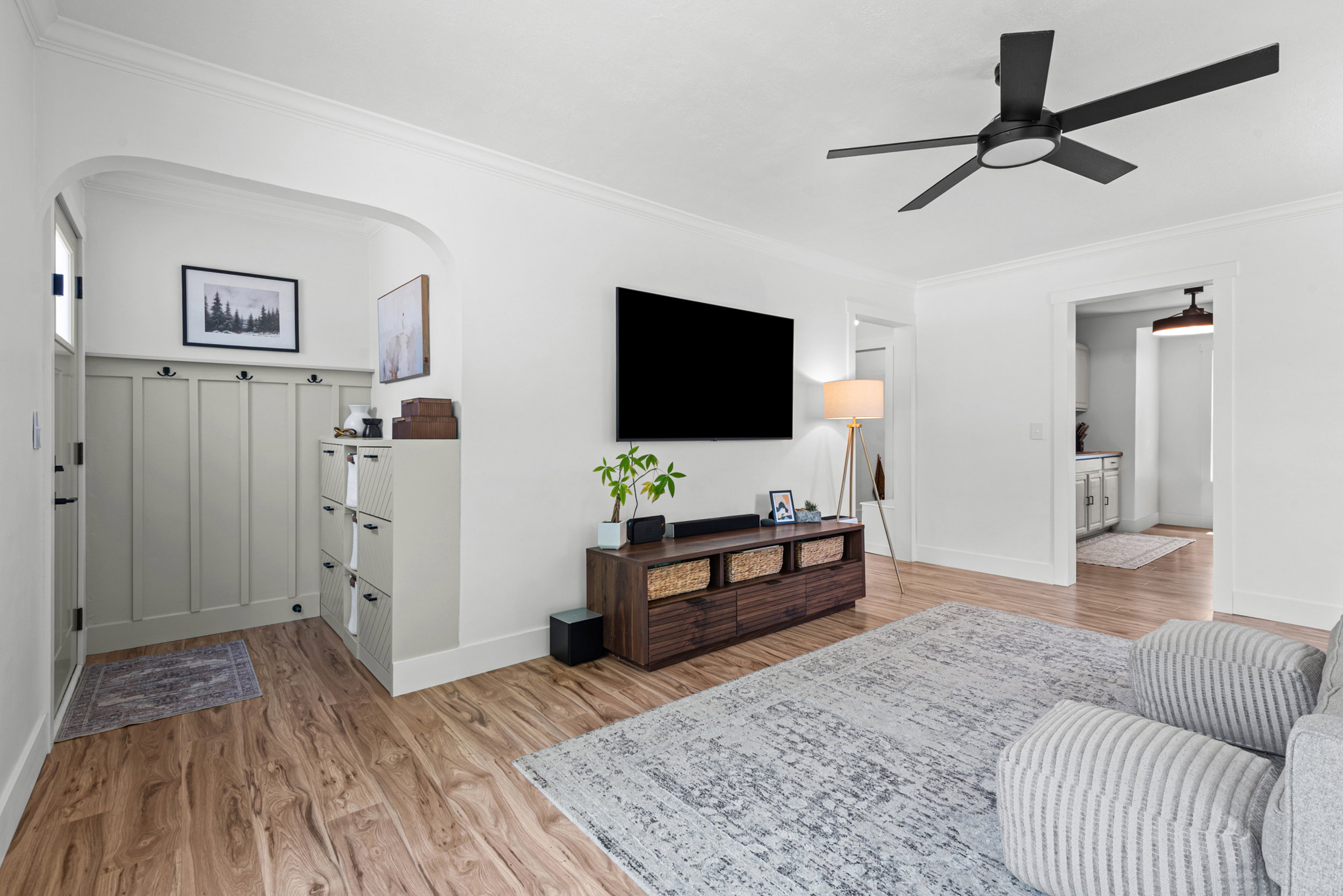 Spacious living area featuring wood-finish flooring, a modern black ceiling fan, and recessed archways