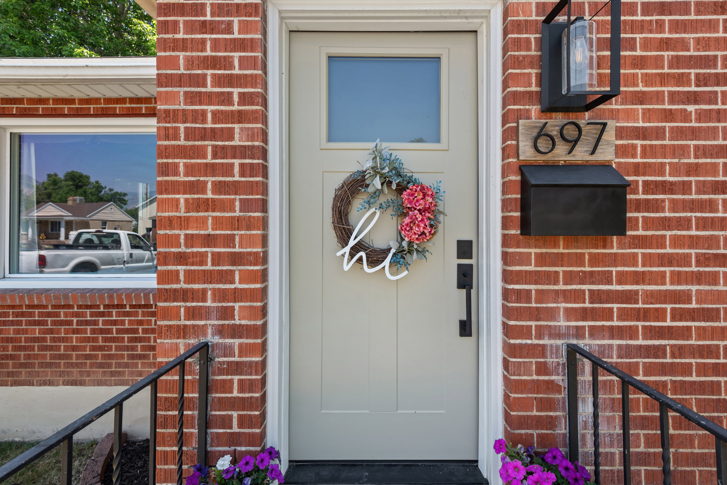 Red brick exterior with a light-colored entry door featuring a transom window, contemporary black hardware, and a coordinating wall-mounted light fixture