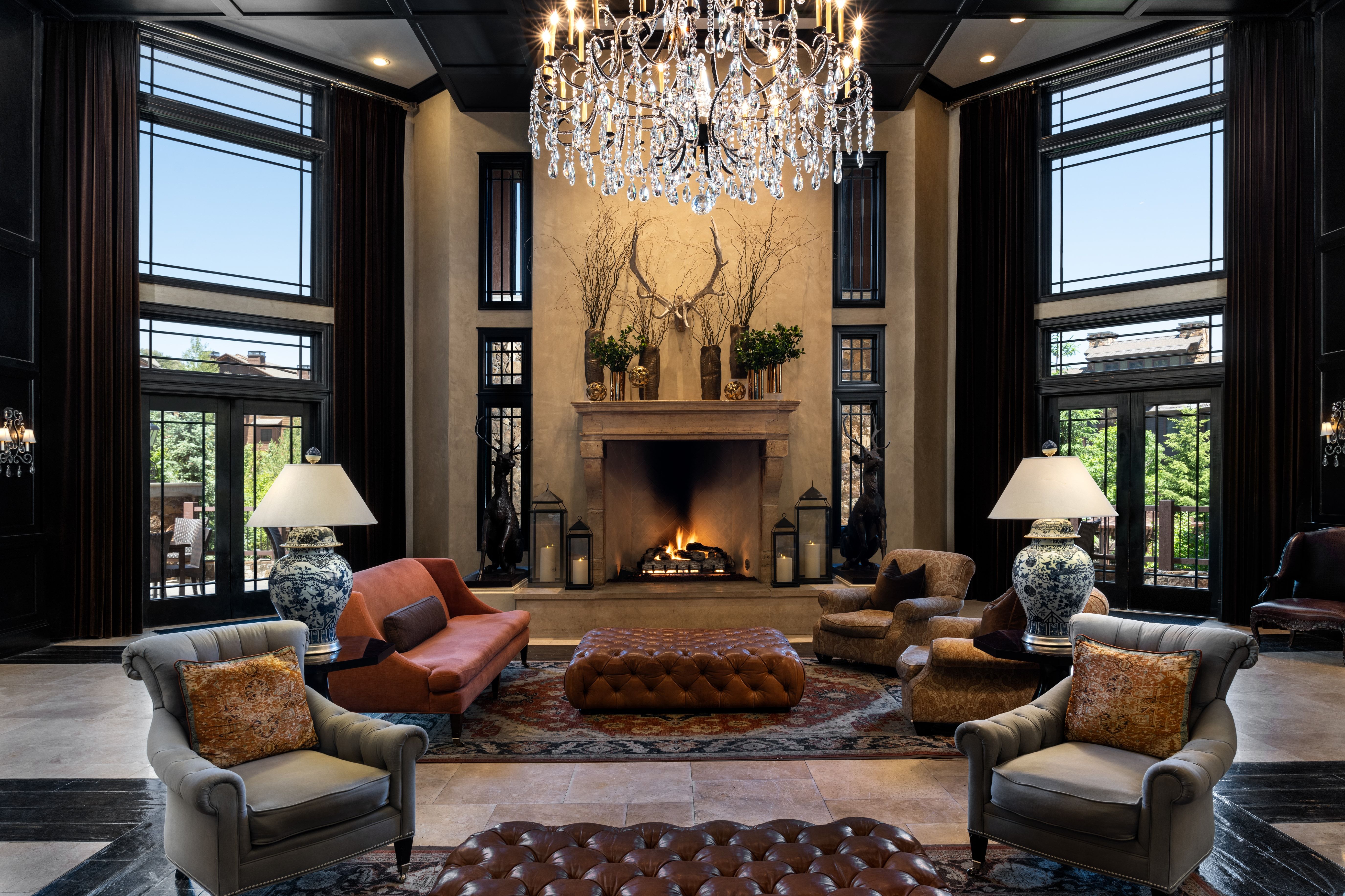 Grand living area featuring a central fireplace with a stone mantel, soaring ceilings, and a crystal chandelier
