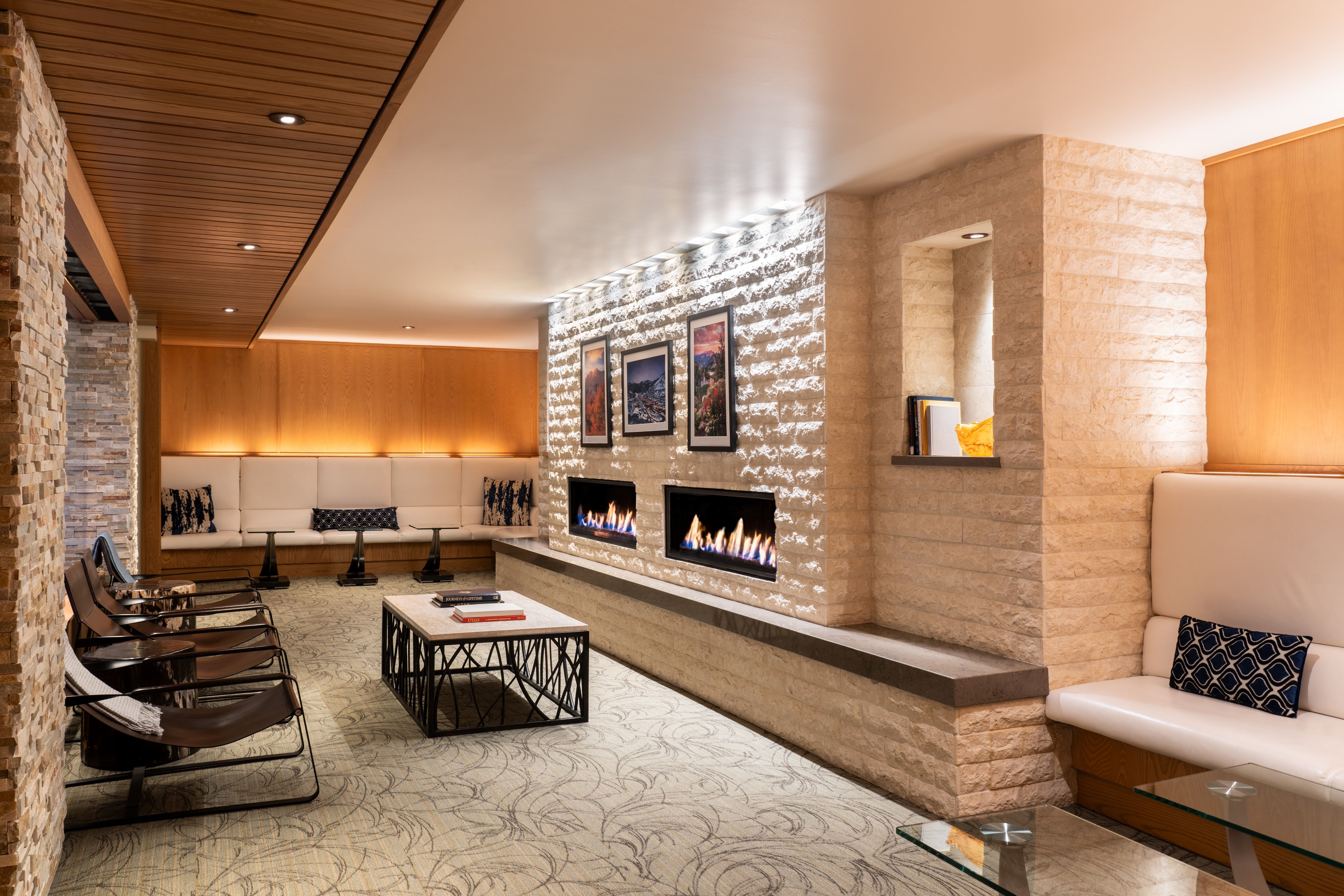 Lounge area featuring a stacked stone accent wall with two linear fireplaces, wood paneling, recessed lighting, and built-in bench seating