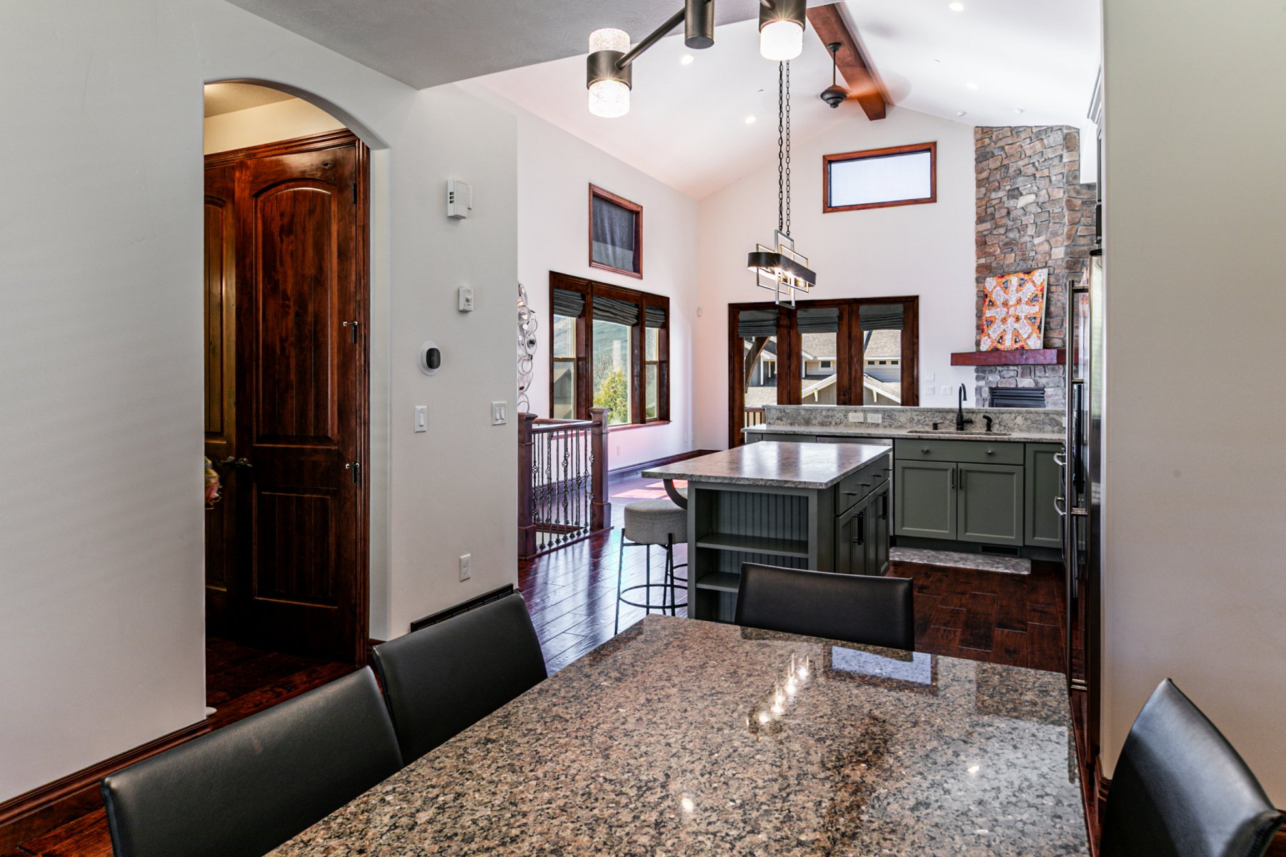 Kitchen and dining area featuring a granite-topped island, dark wood-finish flooring, vaulted ceilings, and stone accent wall