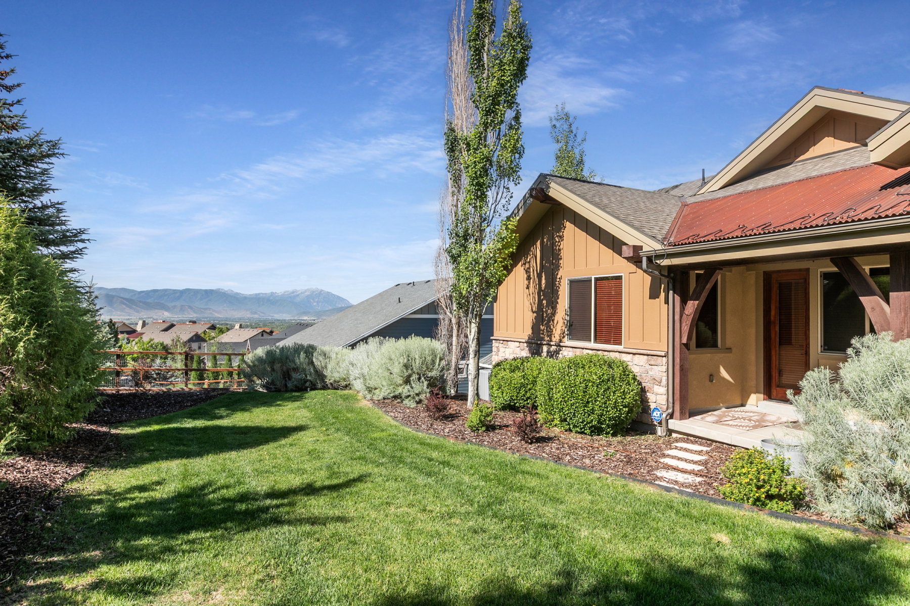 Expansive lawn with surrounding landscaping, featuring stone veneer and vertical siding accents