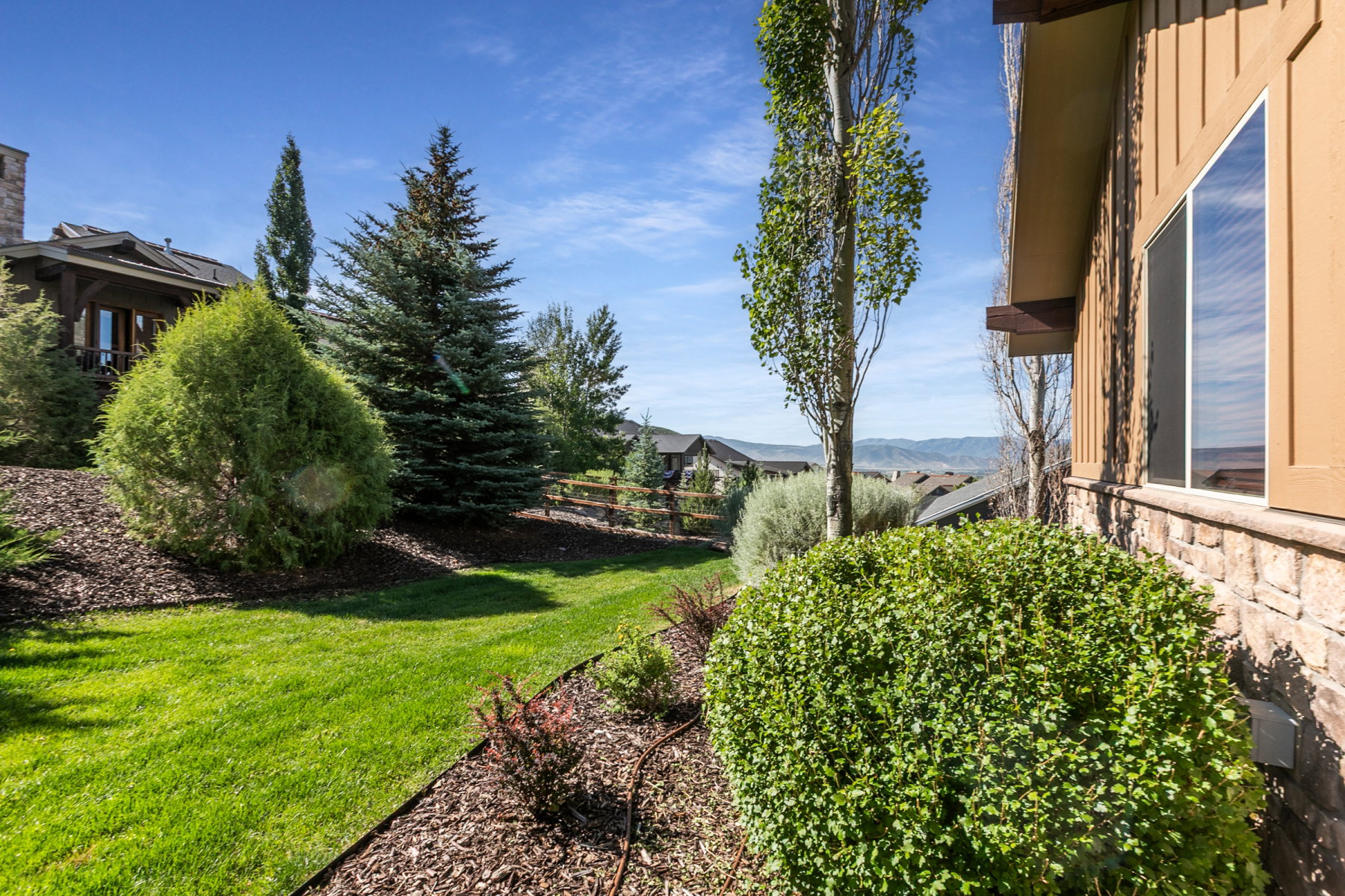 Stone and siding exterior featuring a corner window, mature landscaping, and an expansive lawn