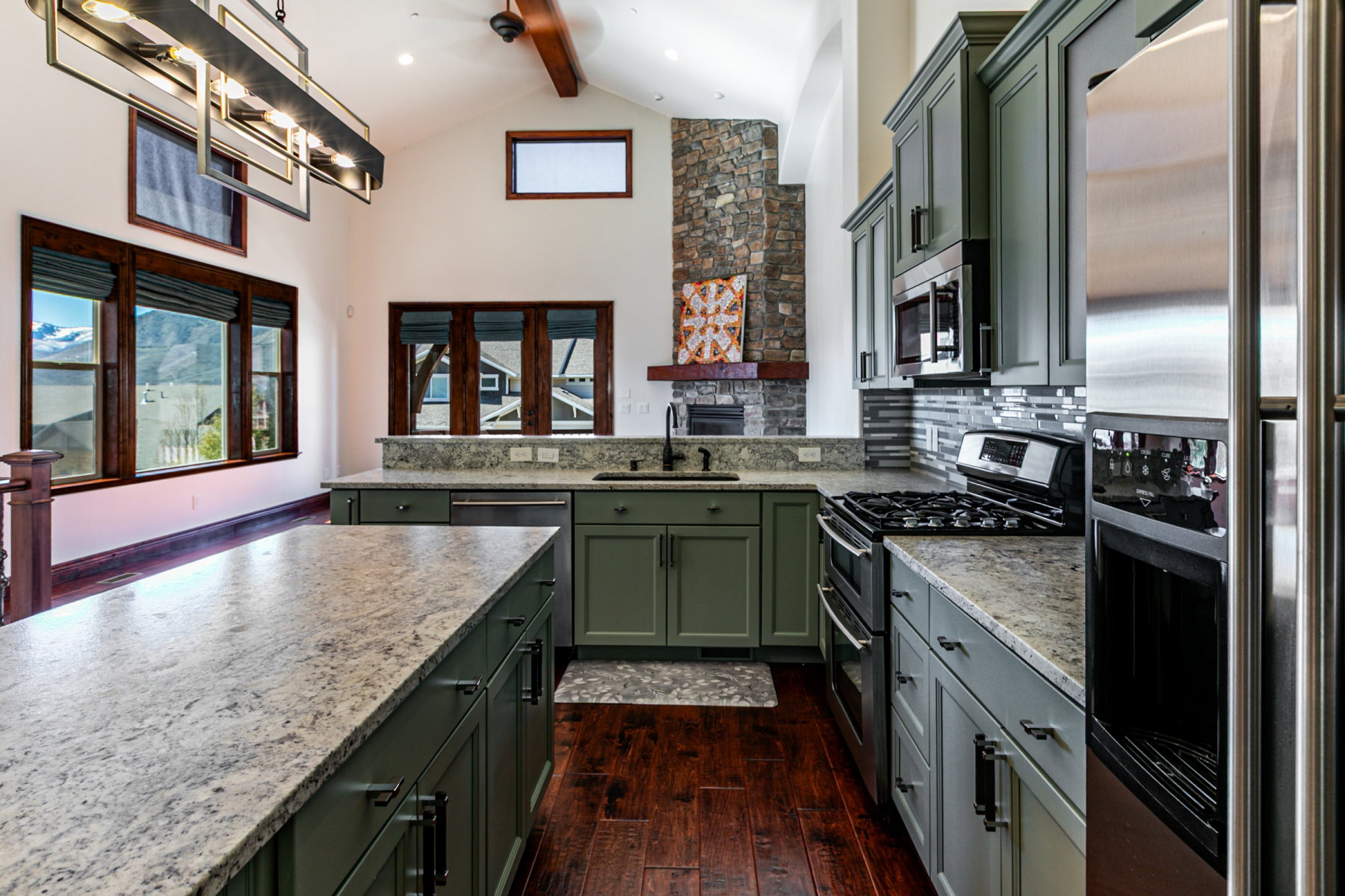 Kitchen featuring an expansive island with a light-toned countertop, contrasting green cabinetry, stainless steel appliances, and rich wood-finish flooring