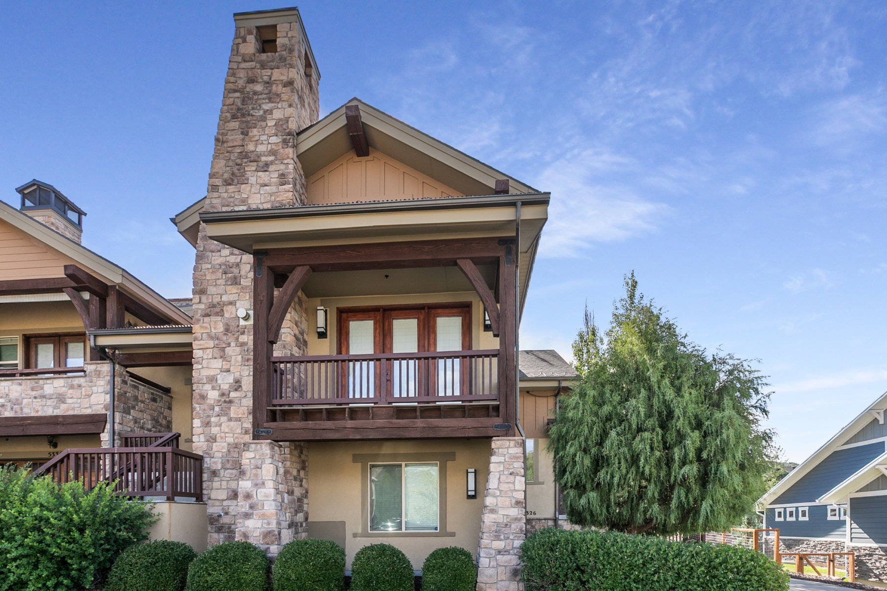 Stone and stucco exterior featuring a prominent stone chimney, wood-beam balcony, and double French doors