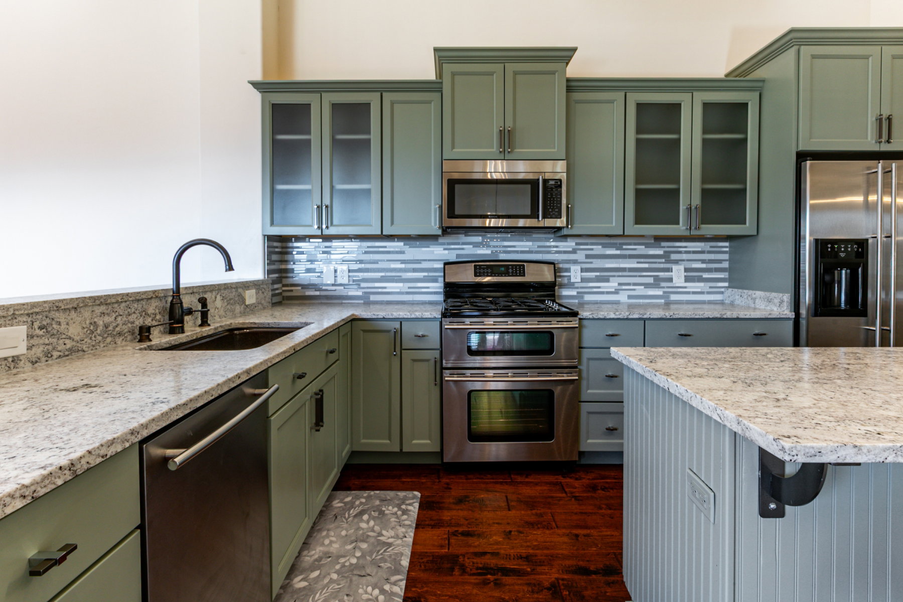 Kitchen featuring sage green cabinetry, stone countertops, stainless steel appliances, a tile backsplash, and wood-finish flooring