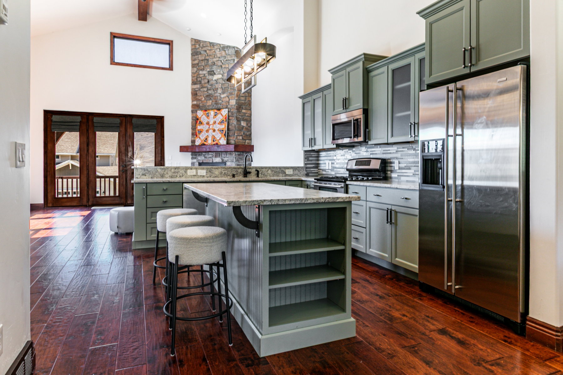 Open-concept kitchen featuring sage-toned cabinetry, stainless steel appliances, and wood-finish flooring