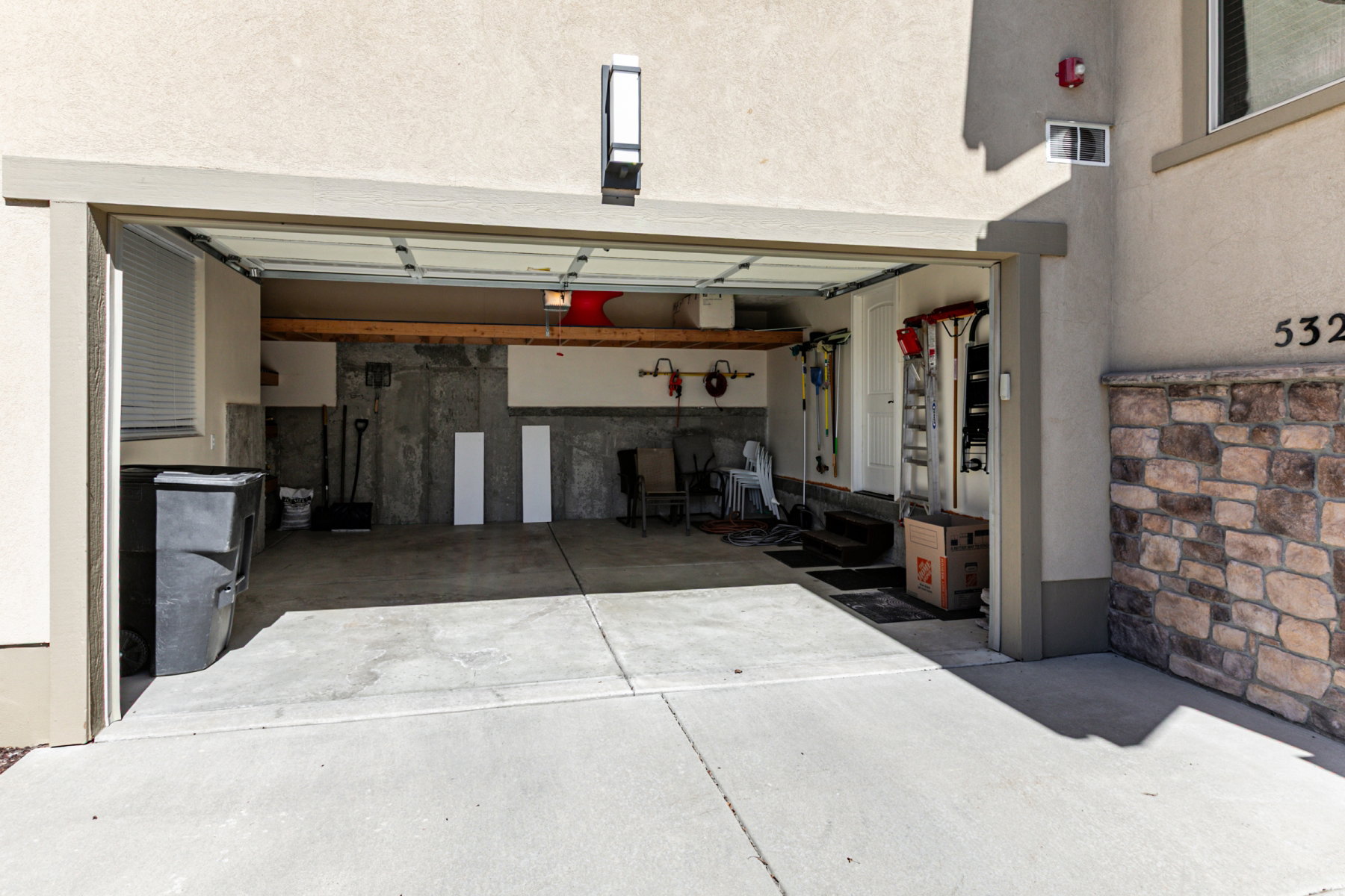 Attached garage with an overhead door, smooth concrete flooring, and an exterior wall featuring stone veneer and stucco finishes