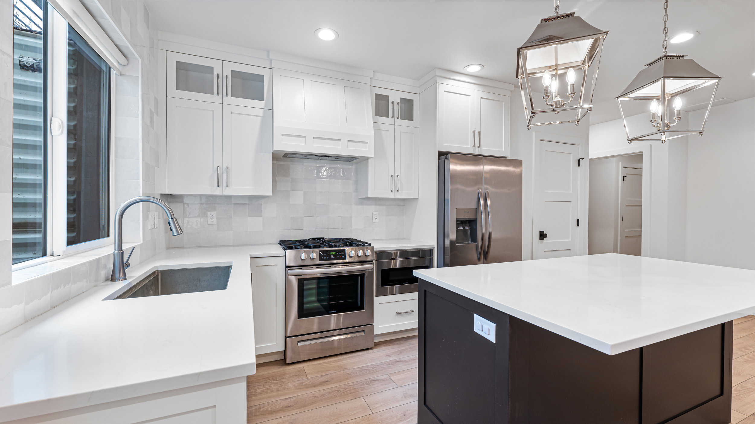 Modern kitchen featuring white cabinetry, stainless steel appliances, a center island with a white countertop, wood-finish flooring, and two suspended lantern-style light fixtures