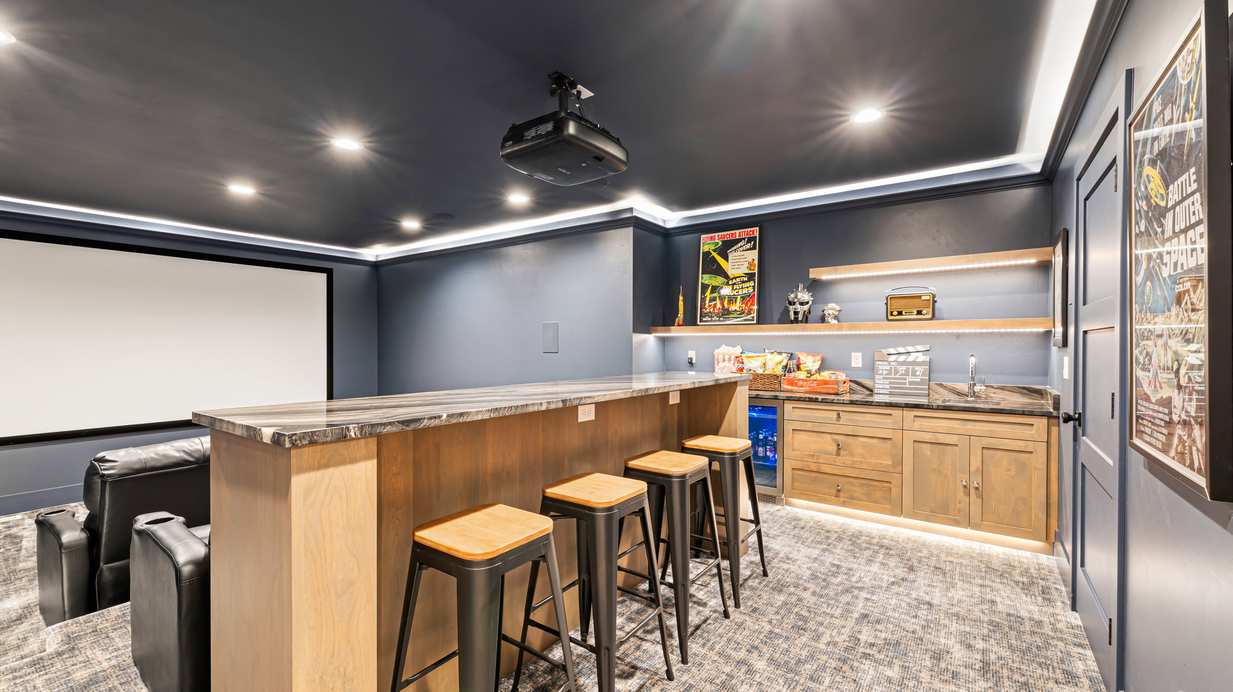 Custom home theater featuring a large projection screen, built-in wet bar with wood-finish cabinetry, and recessed lighting