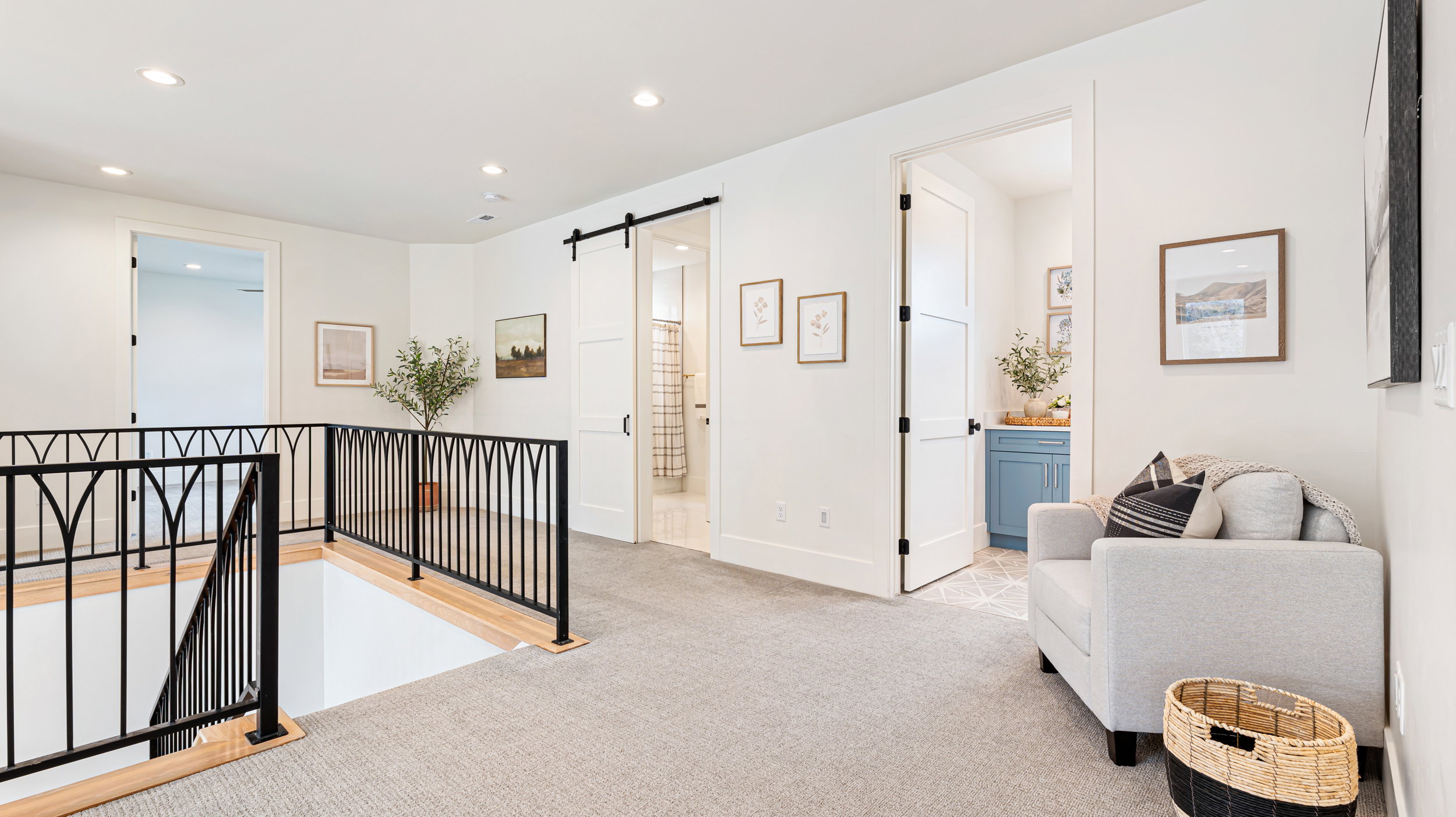 Upper-level landing featuring light-colored carpeting, recessed lighting, and a decorative black metal railing