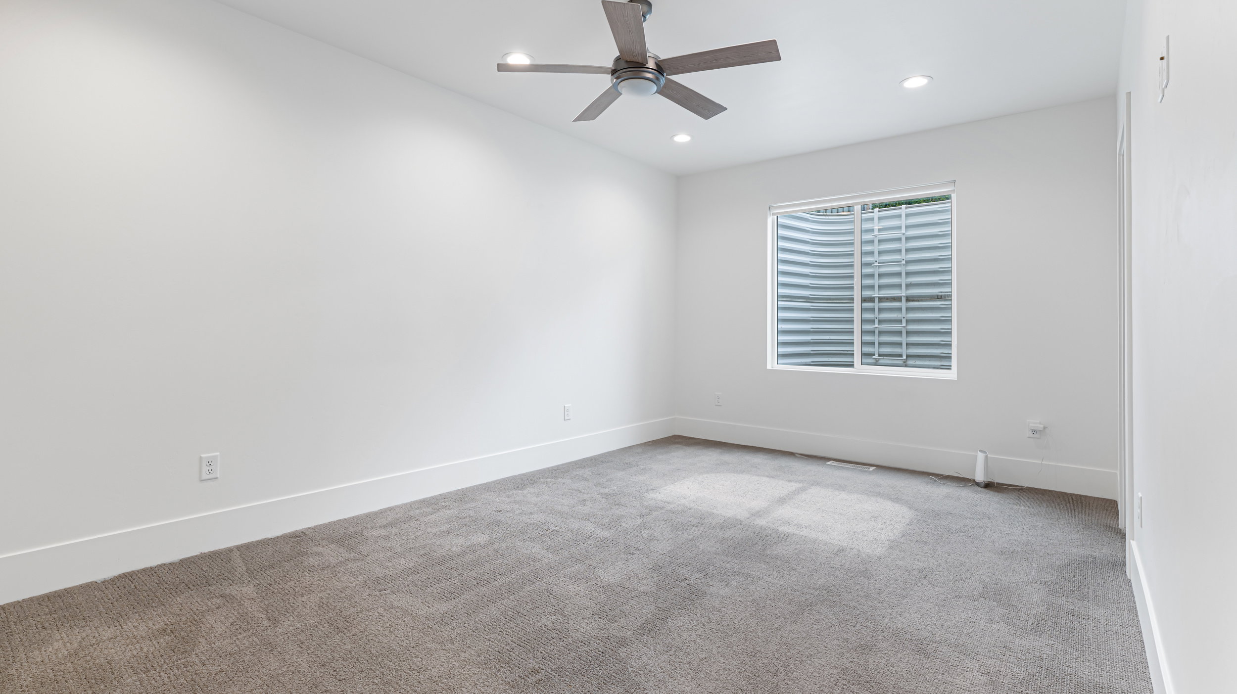Spacious room featuring neutral carpeting, a modern ceiling fan, recessed lighting, and a window with a window well
