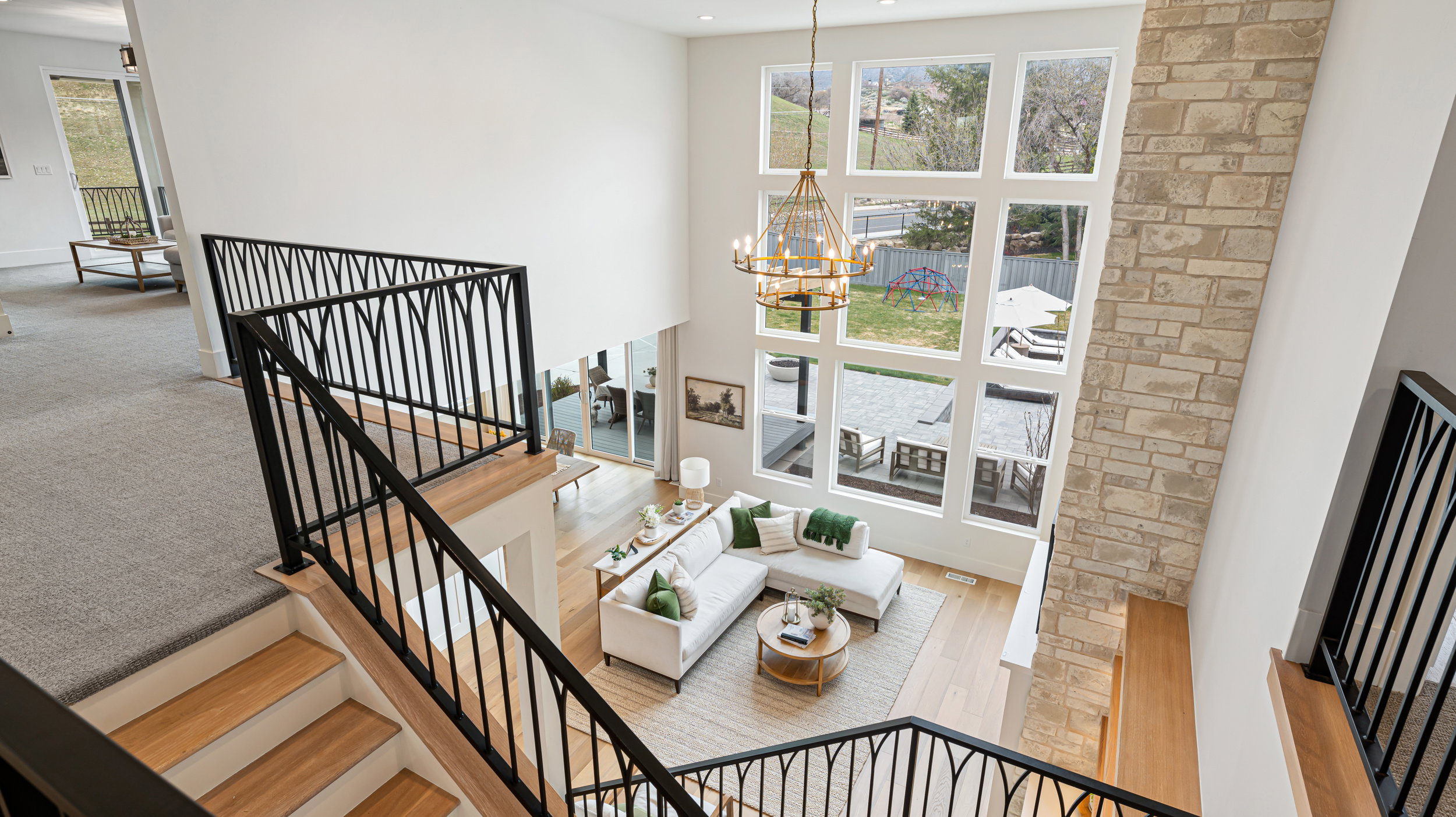 Two-story living area featuring a stacked stone fireplace column, a multi-pane picture window wall, and a gold-tone chandelier