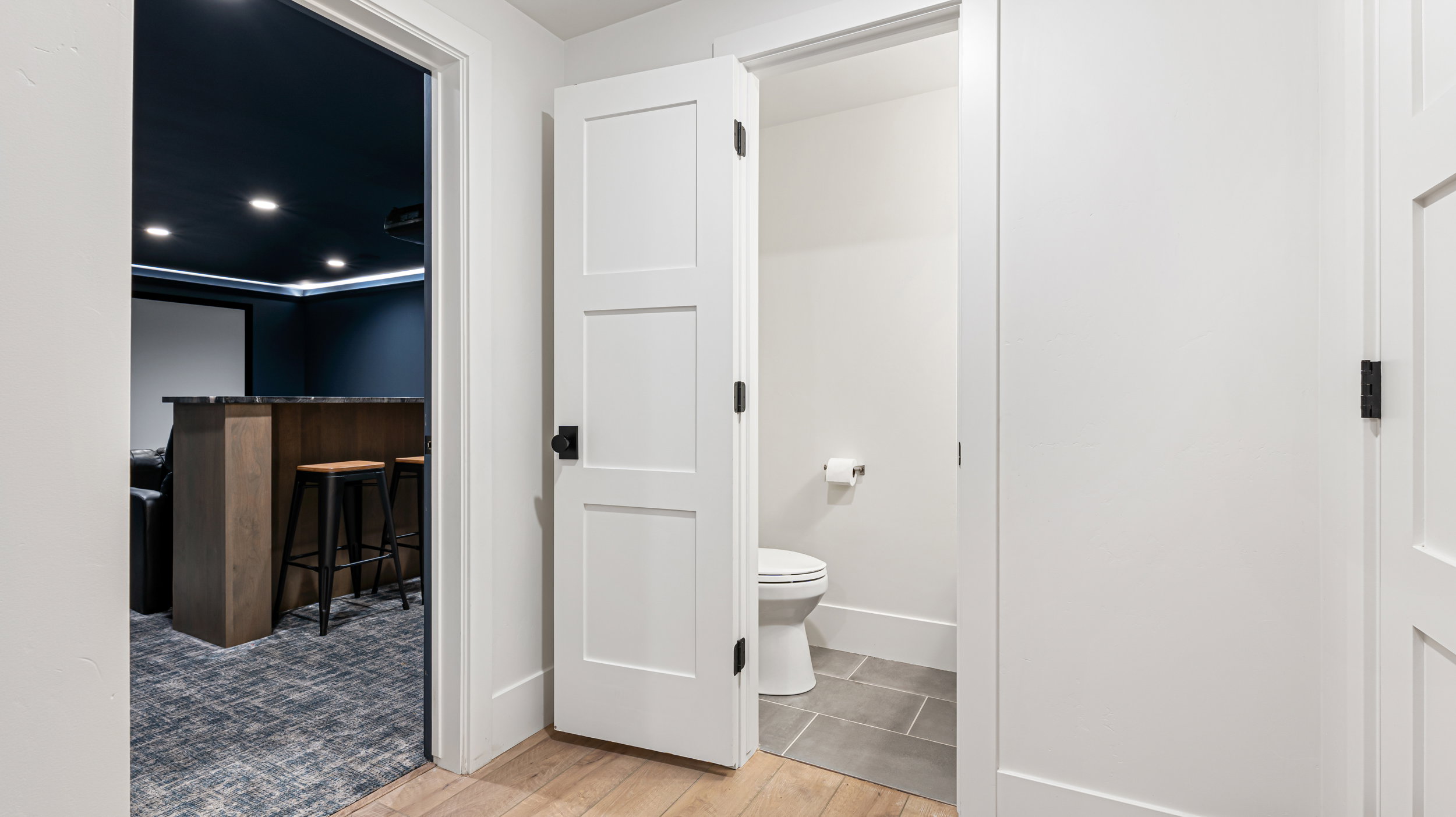 Hallway with light wood-finish flooring, white paneled doors, and matte black hardware