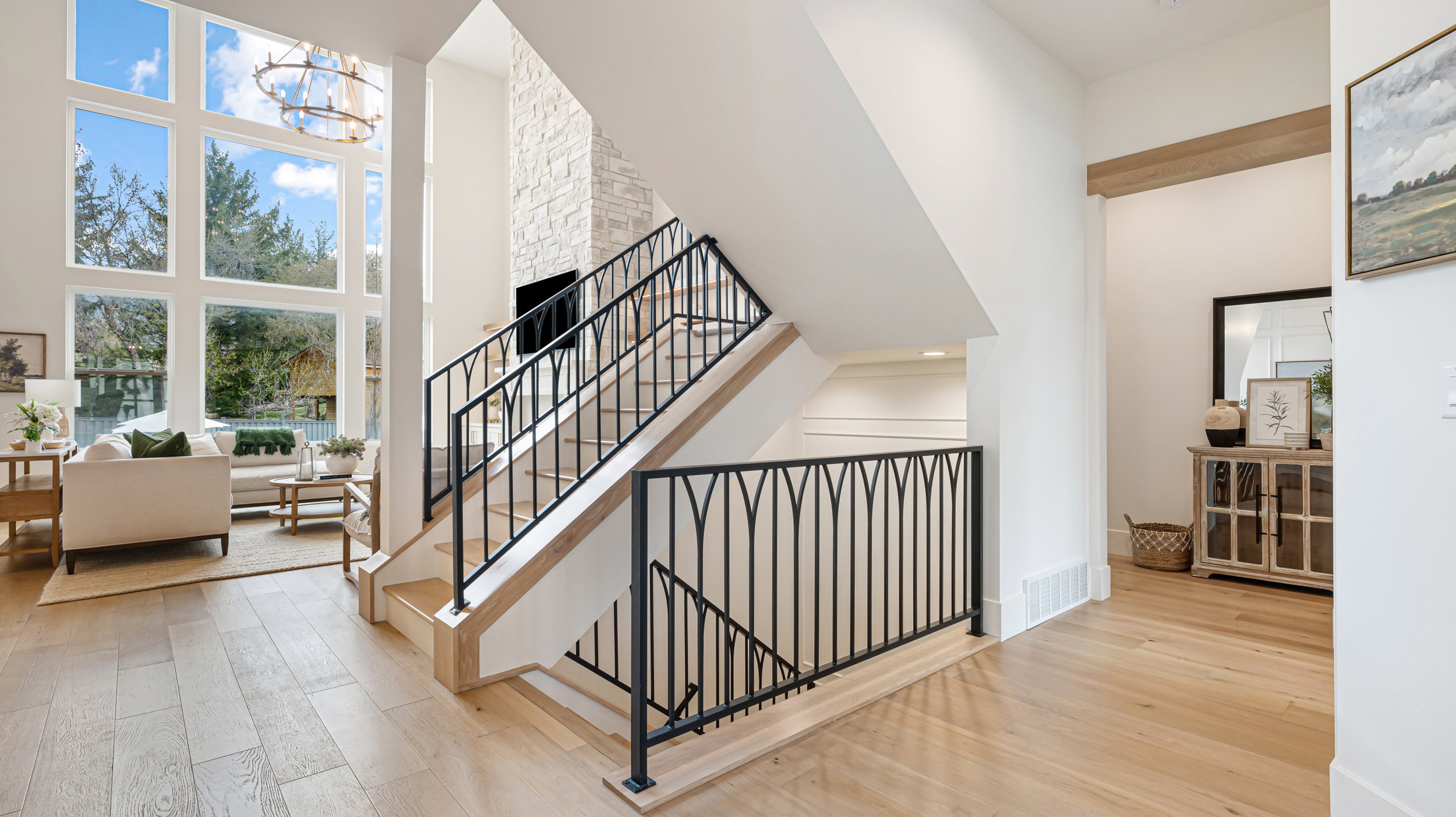 Open-concept living space with light wood-finish flooring, a contemporary staircase featuring black metal balusters, and a two-story stone accent wall