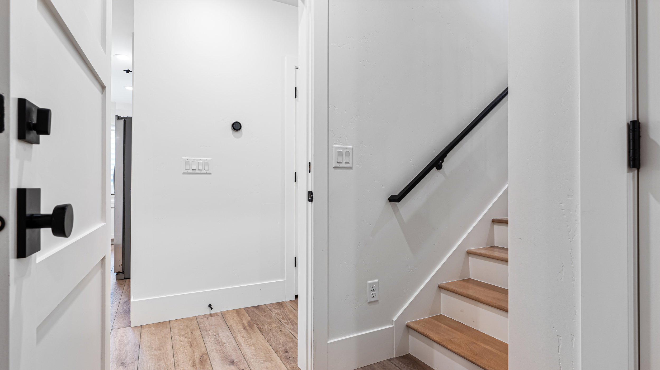 Hallway featuring wood-finish flooring, white walls, and a staircase with wood treads and a black metal handrail