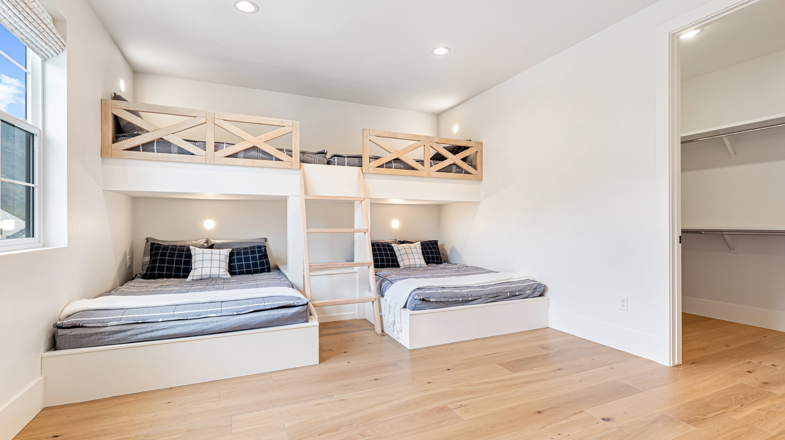 Spacious room featuring light wood-finish flooring, built-in bunk beds with natural wood accents, recessed lighting, and a window with natural light