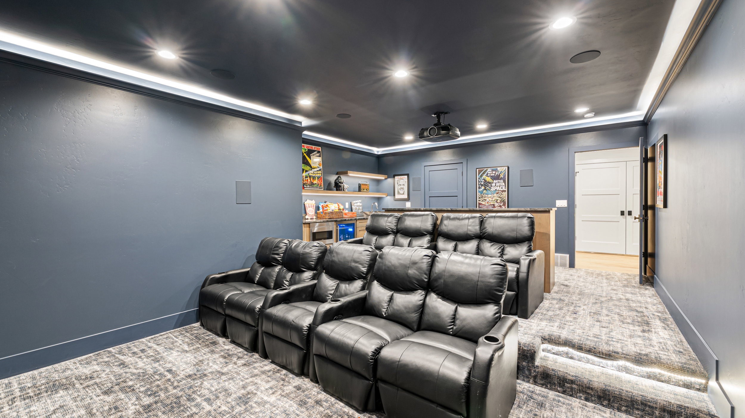 Dedicated media room featuring tiered seating, recessed lighting, accent wall lighting, wall-mounted speakers, and a ceiling-mounted projector