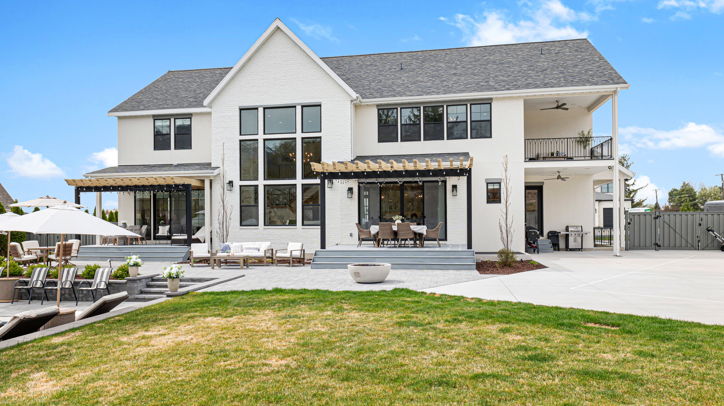 Stately white brick exterior featuring multiple outdoor living spaces, including a spacious patio, dedicated sports court, and an upper-level balcony