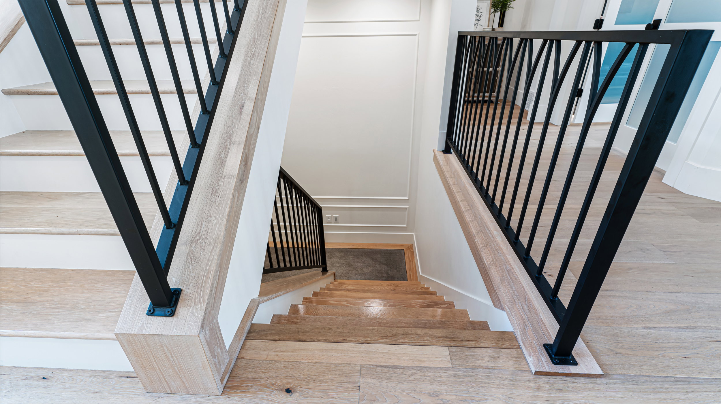 Contemporary staircase featuring black wrought iron balusters and light wood-finish treads