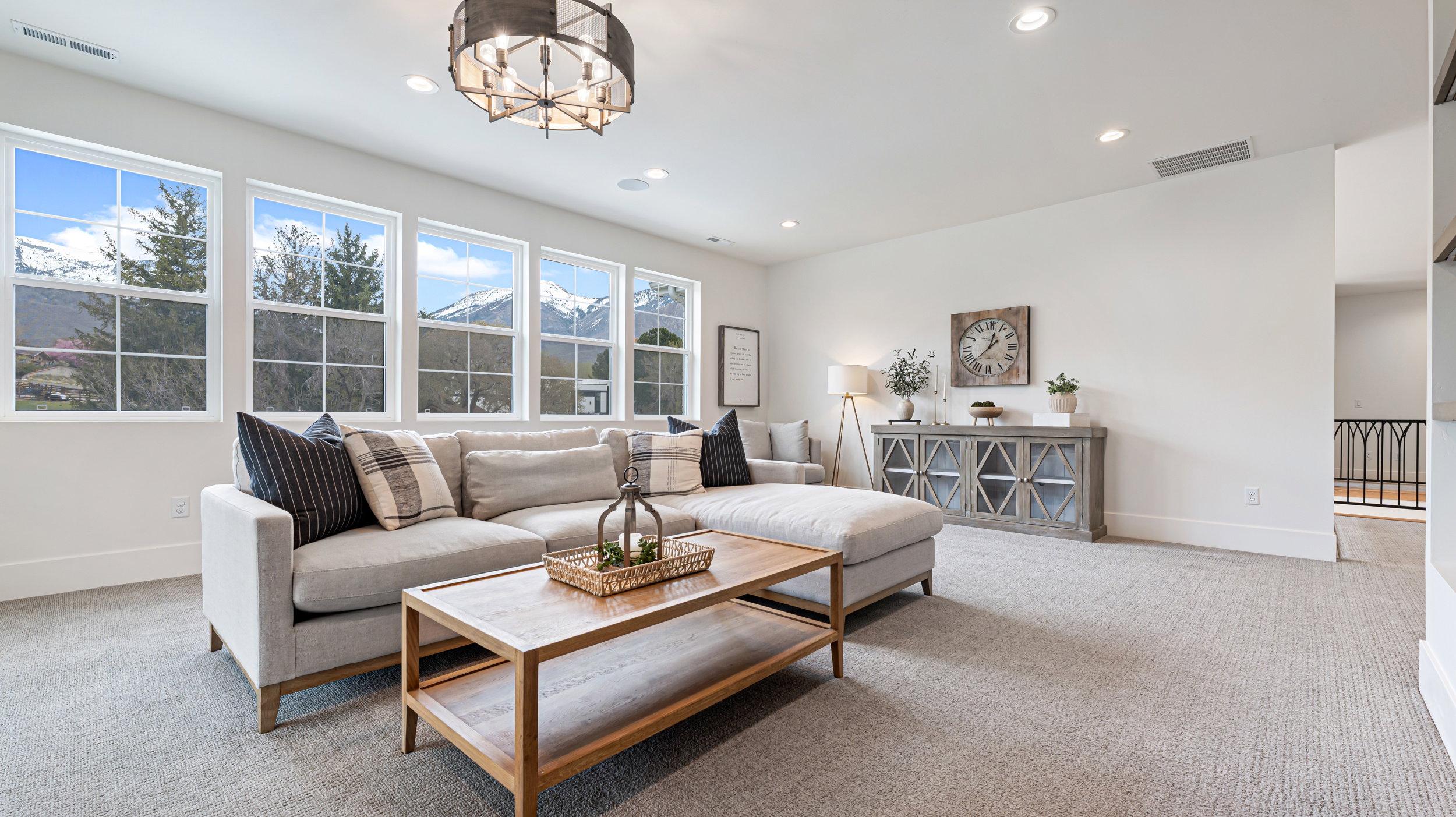 Spacious living area featuring multiple large windows, recessed lighting, an architectural chandelier, neutral carpet, and white baseboards