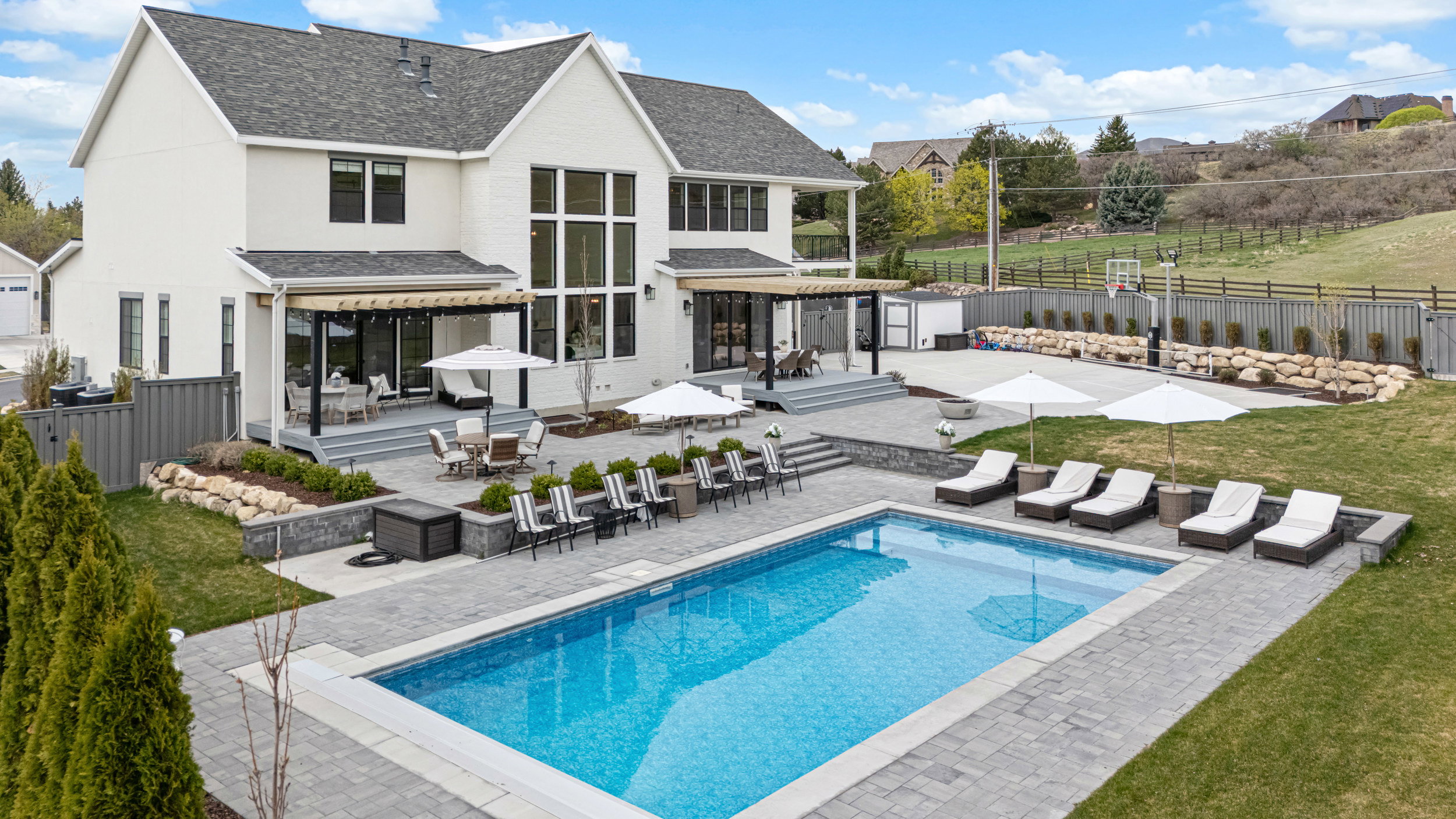 Expansive backyard featuring a rectangular swimming pool with integrated lighting, a large paver patio, and multiple tiered landscaping beds