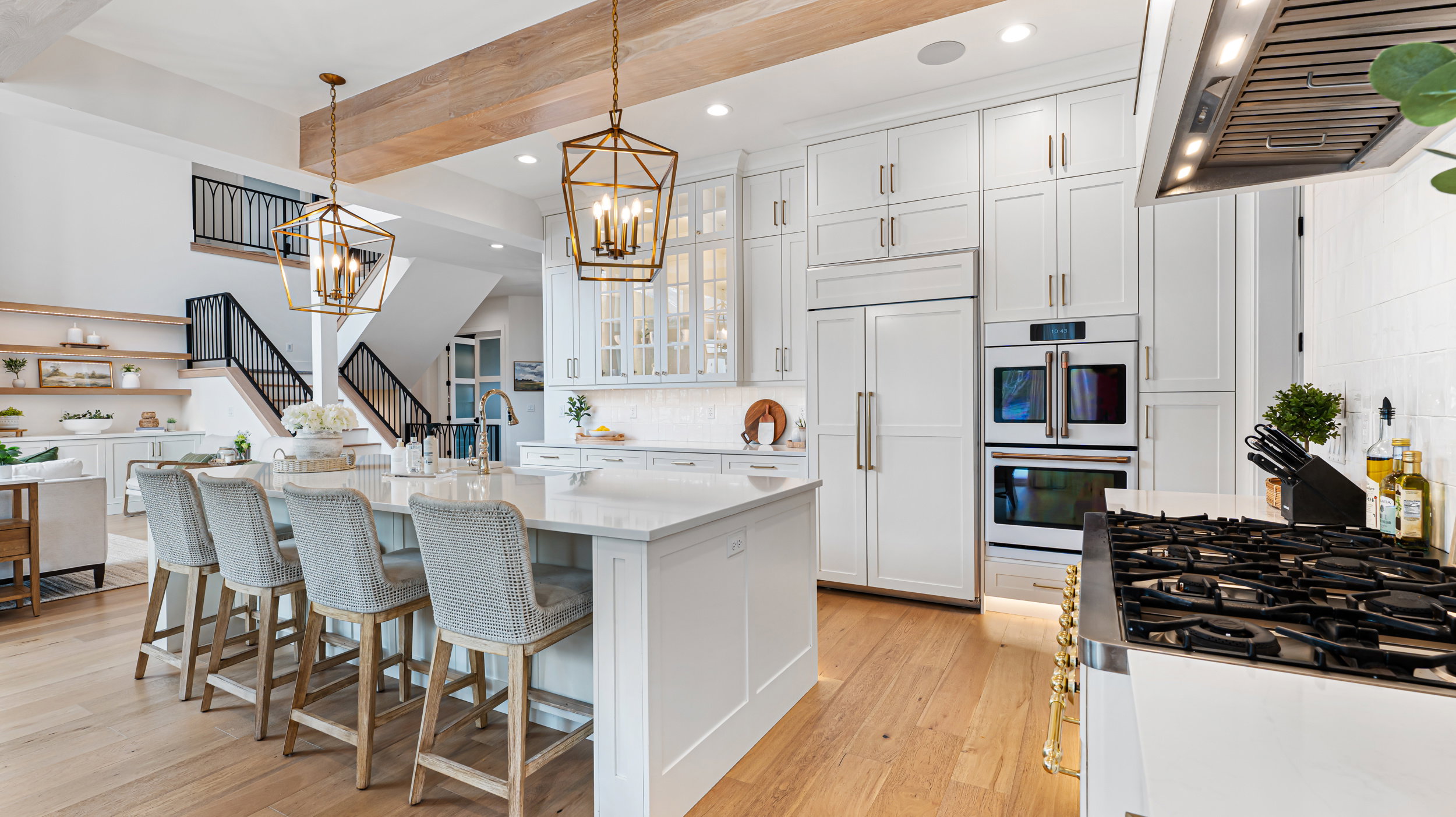 Gourmet kitchen featuring a large central island with seating, stainless steel appliances including a built-in oven and gas range, white cabinetry with display uppers, and wood-finish flooring