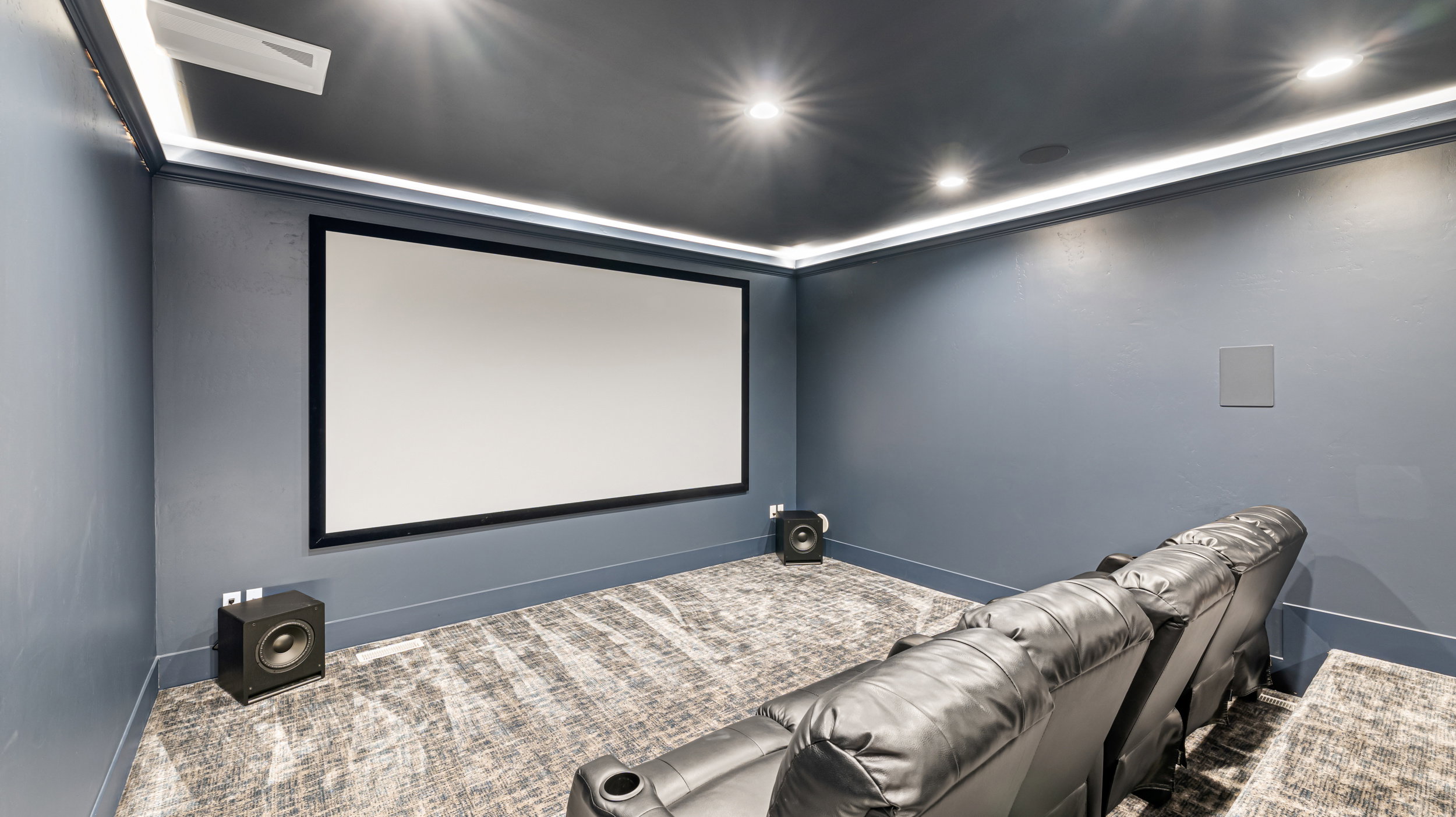 Dedicated media room featuring a large projection screen, recessed lighting, cove lighting, built-in wall speaker, and dark blue wall finishes