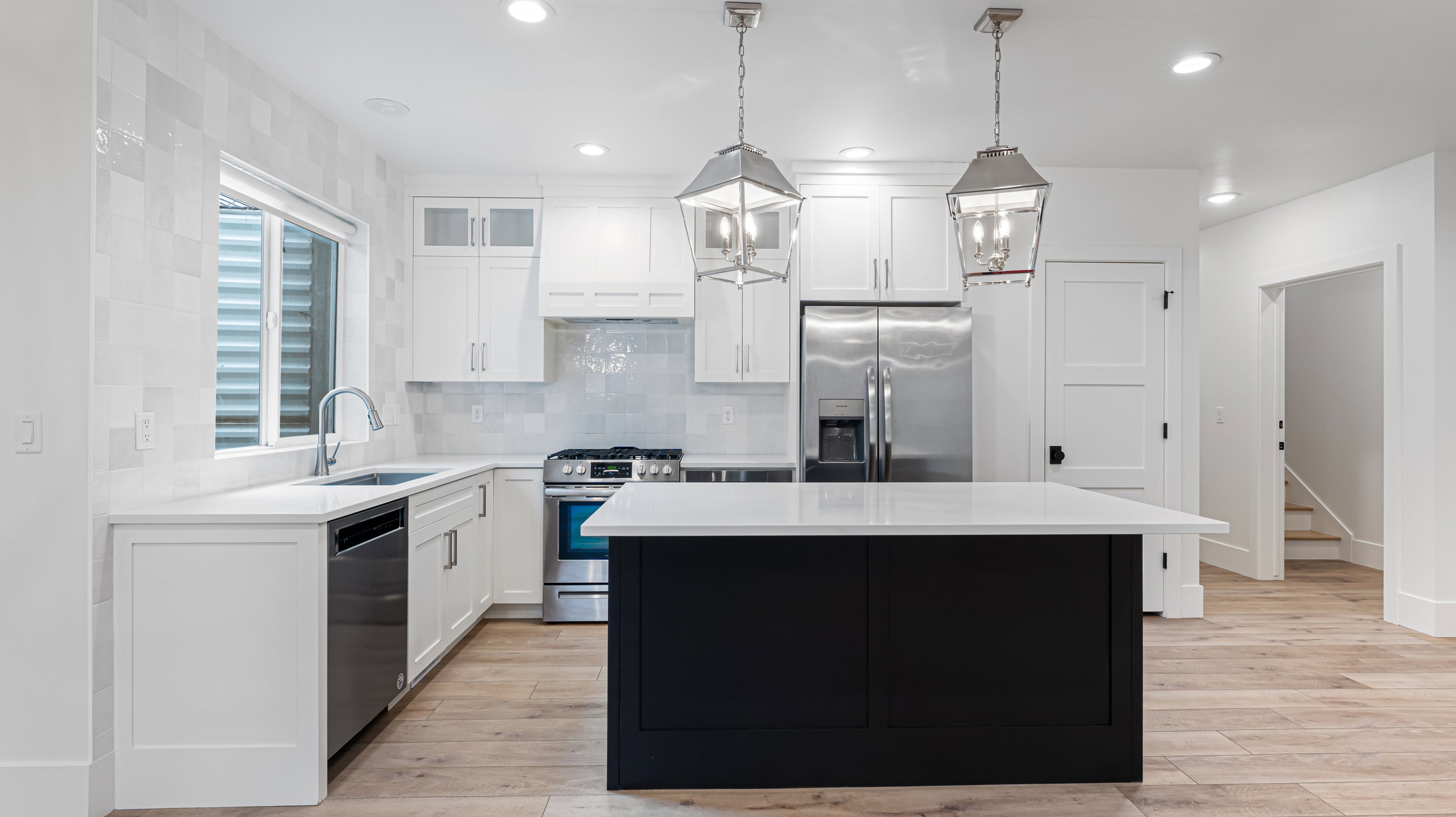 Modern kitchen featuring a contrasting black island with a white countertop, stainless steel appliances, white cabinetry, and wood-finish flooring