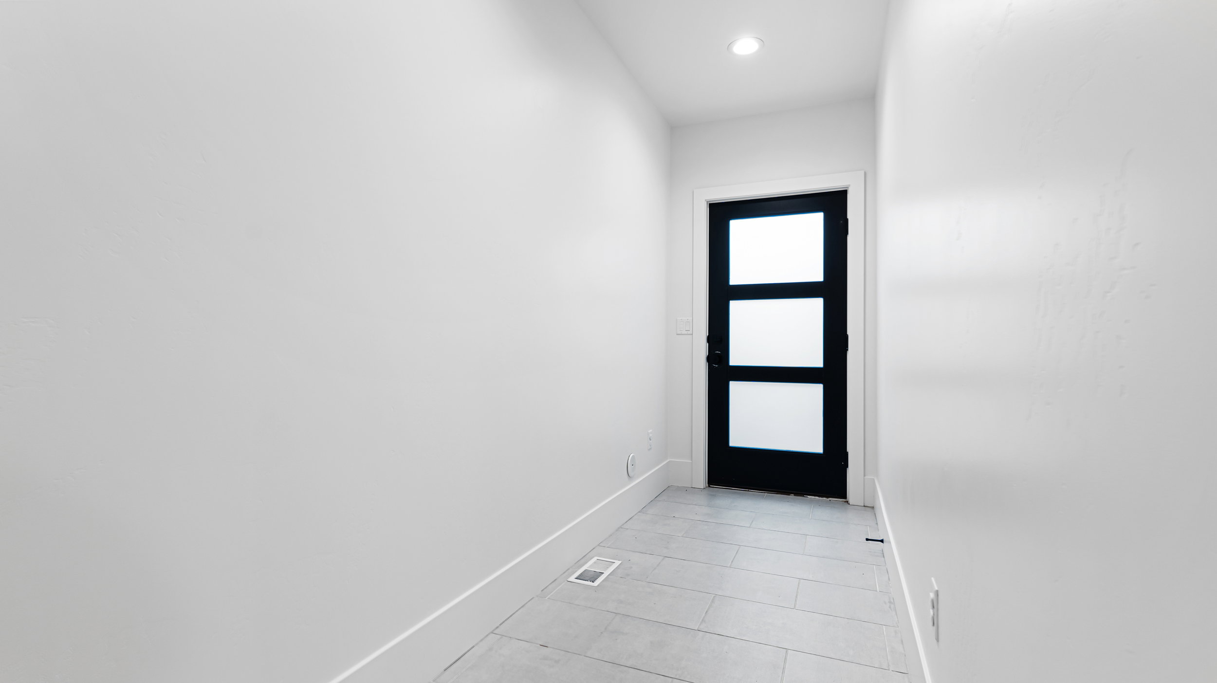 Contemporary black door with three frosted glass panels, recessed ceiling lighting, and light grey rectangular tile flooring