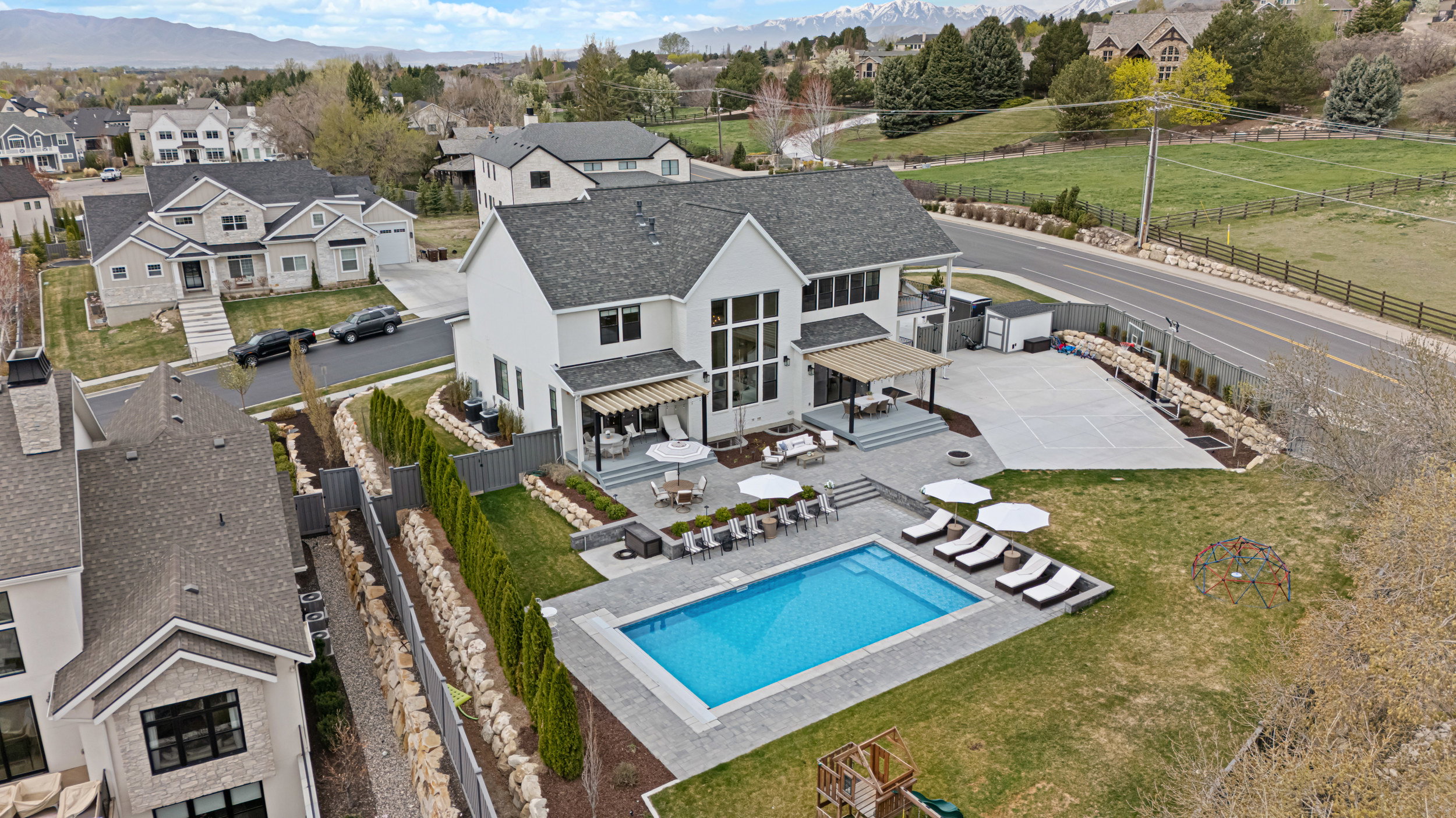 Contemporary residence with a rectangular swimming pool, spacious paved patio, multi-level outdoor entertaining areas, and an expansive sports court