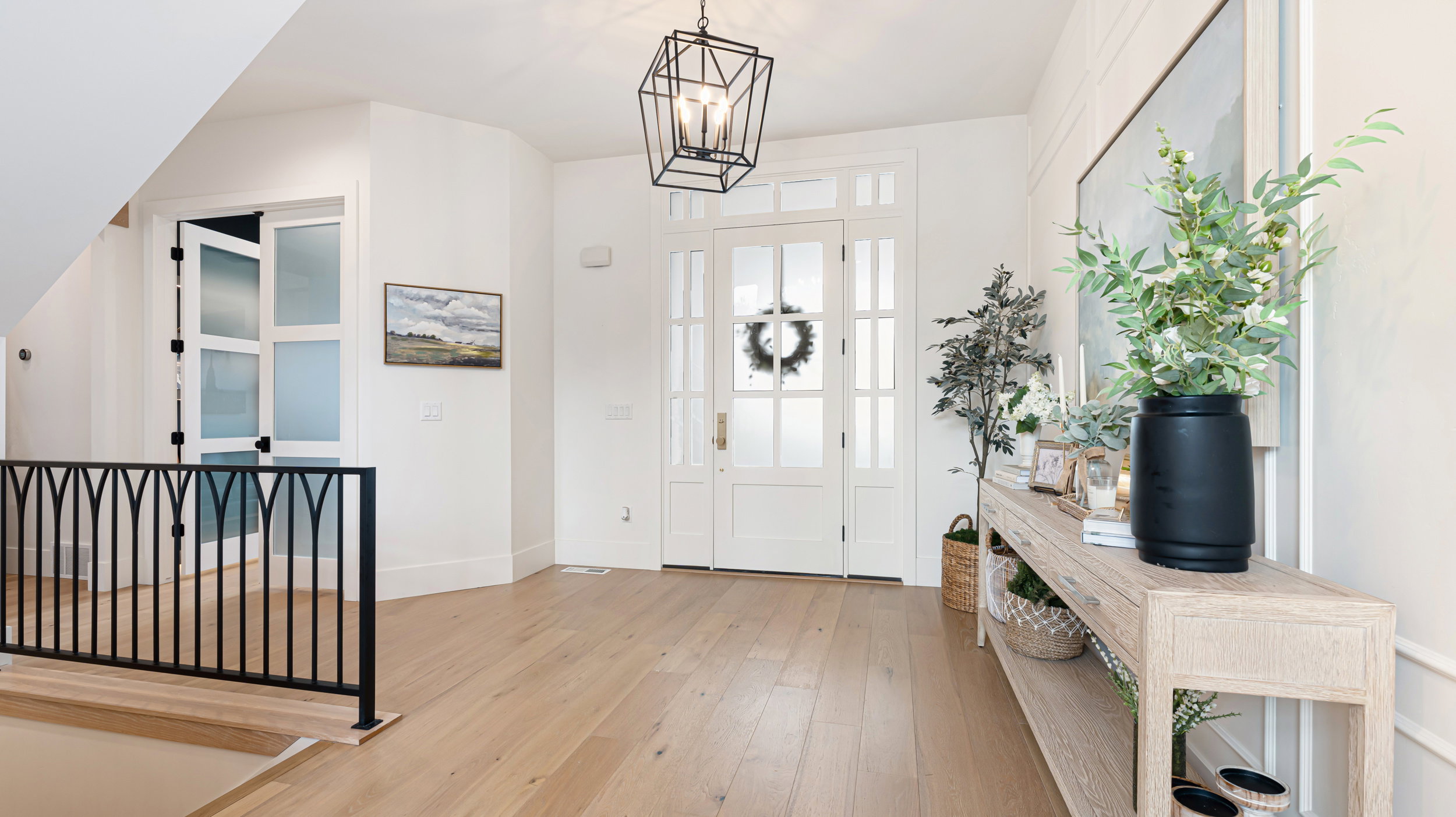 Spacious entryway featuring wood-finish flooring, a contemporary geometric pendant light fixture, and a paneled front door with frosted glass