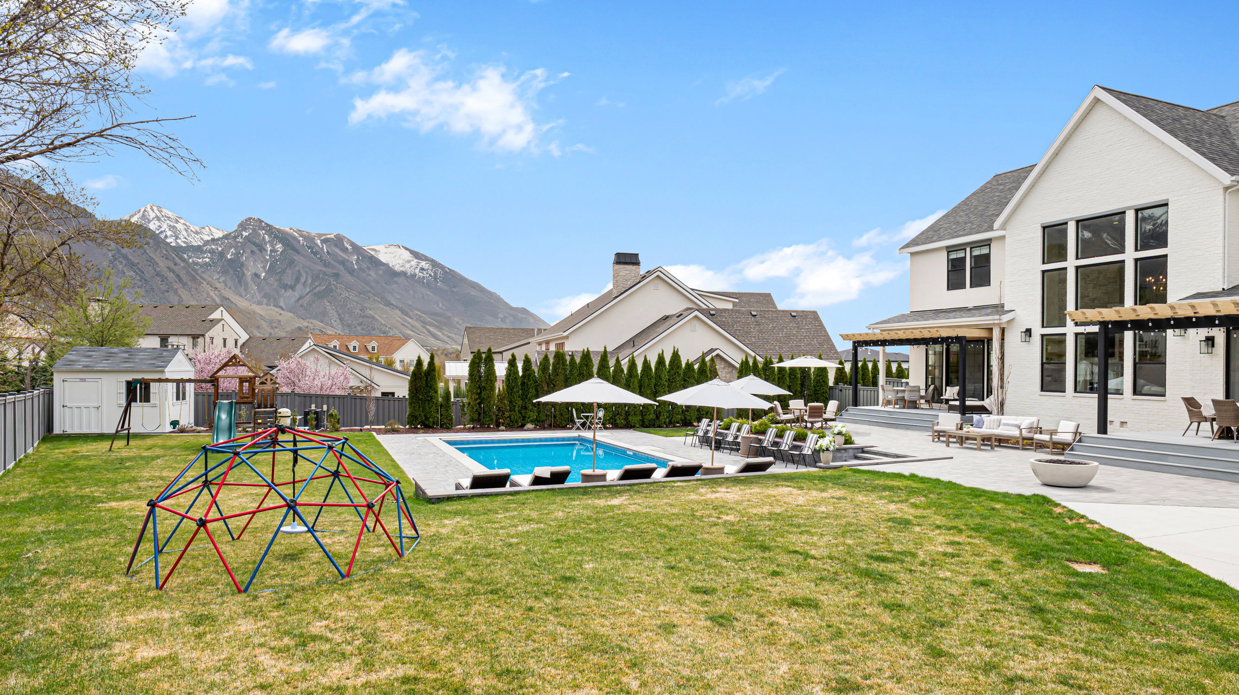 Expansive backyard featuring a rectangular swimming pool, concrete patio, two pergolas, and a manicured lawn