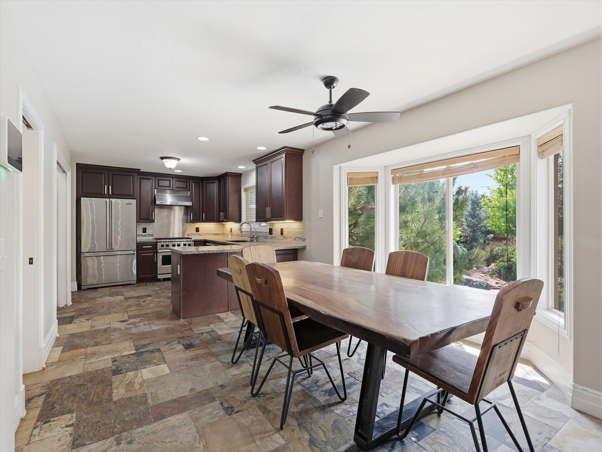Open-concept kitchen and dining area featuring dark wood cabinetry, stainless steel appliances, a center island with granite countertops, and slate tile flooring