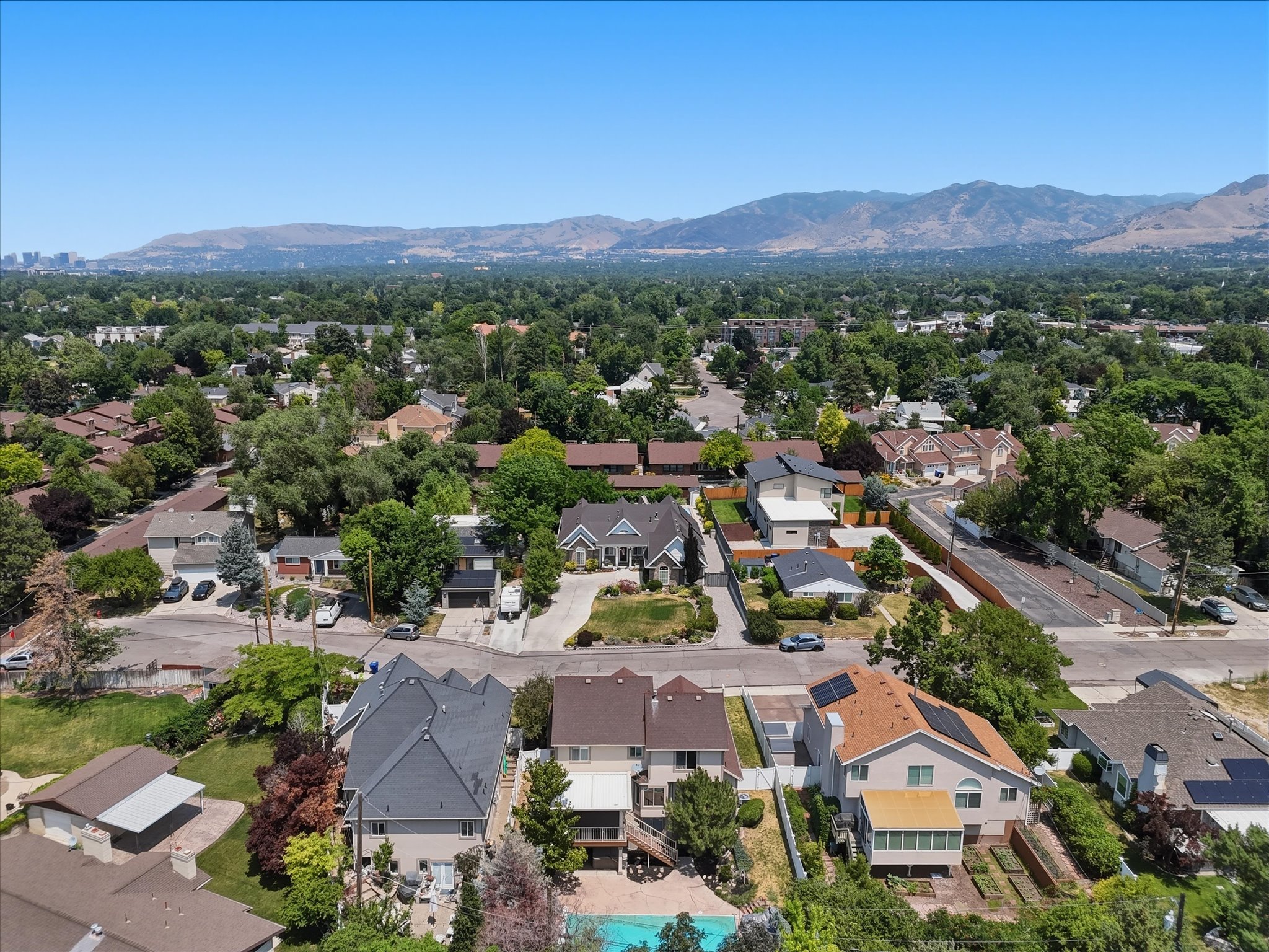 Aerial overview of a residential area featuring established homes with diverse architectural styles, mature trees, and a distant mountain range